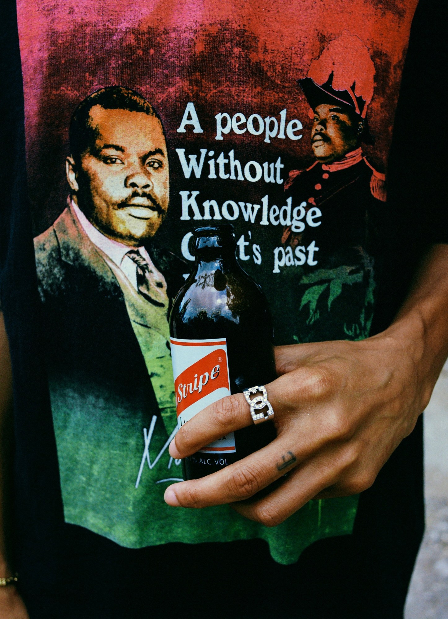 Photograph by Julian Klincewicz of someone holding a red stripe beer and wearing a DCV'87 top that has a Marcus Garvey quote on it