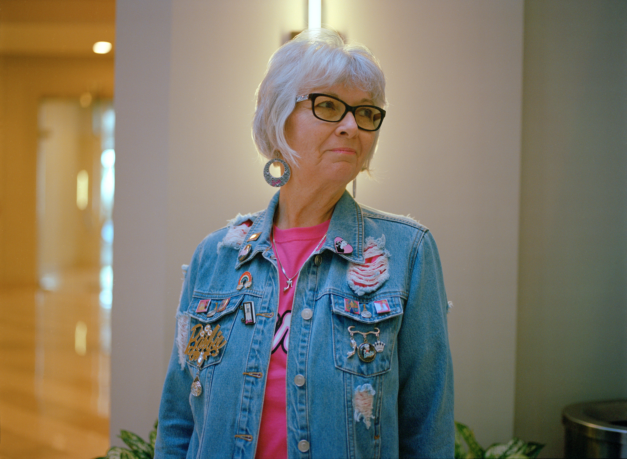 a woman in a pink tee and denim jacket covered in barbie pins