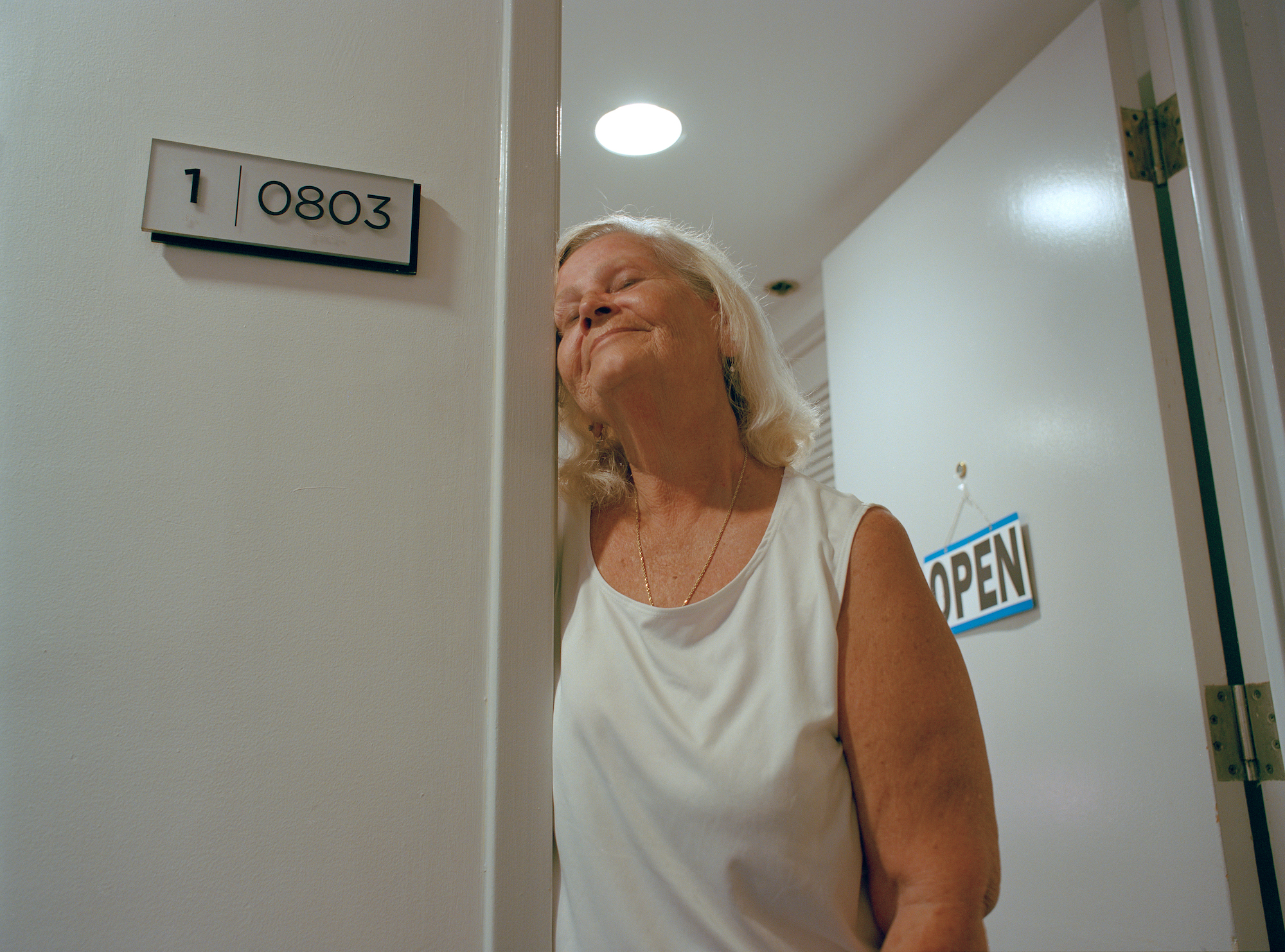 a woman standing in an open door in a white tank top