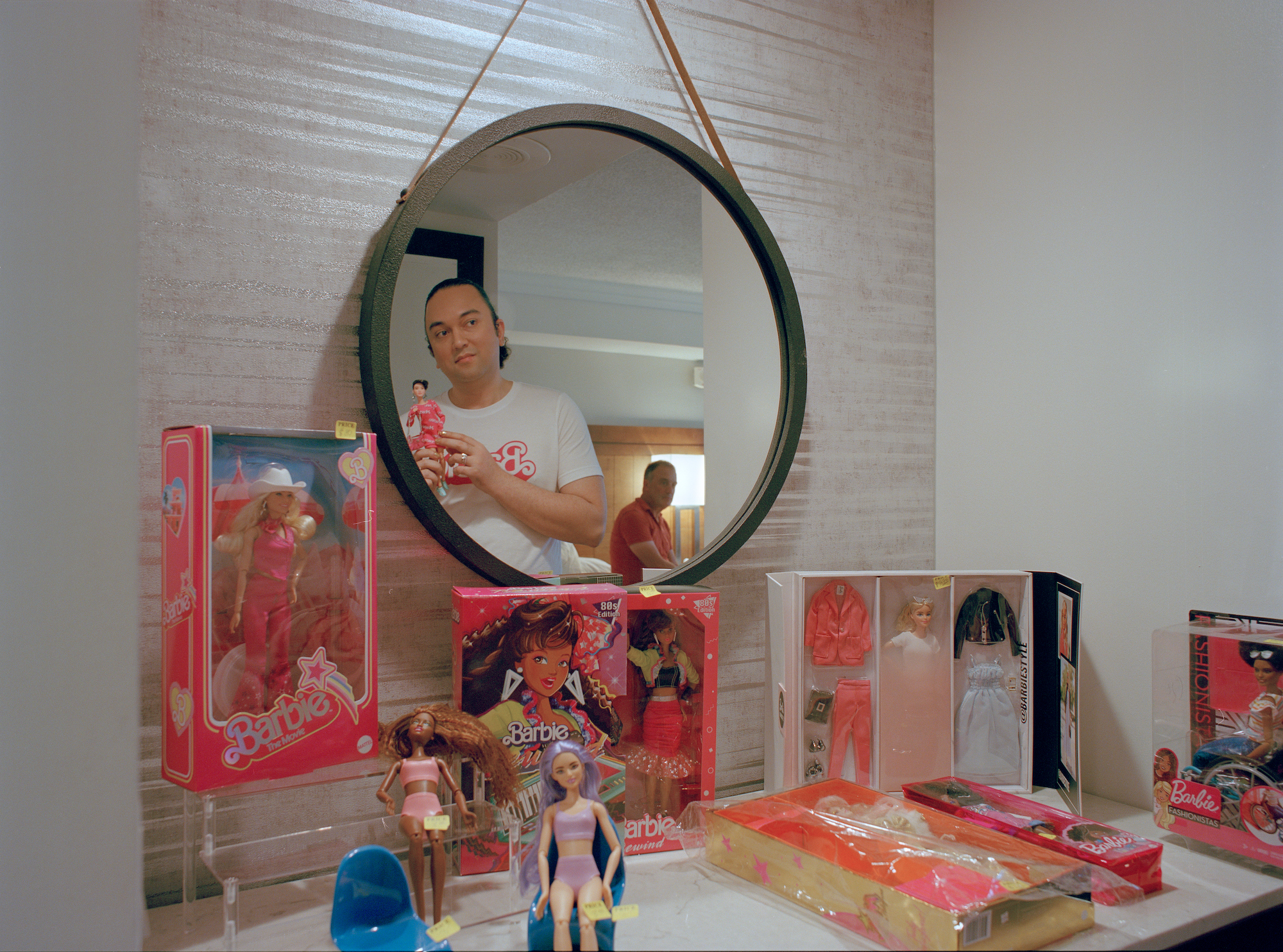 a couple looking into a bathroom mirror surrounded by vintage barbies