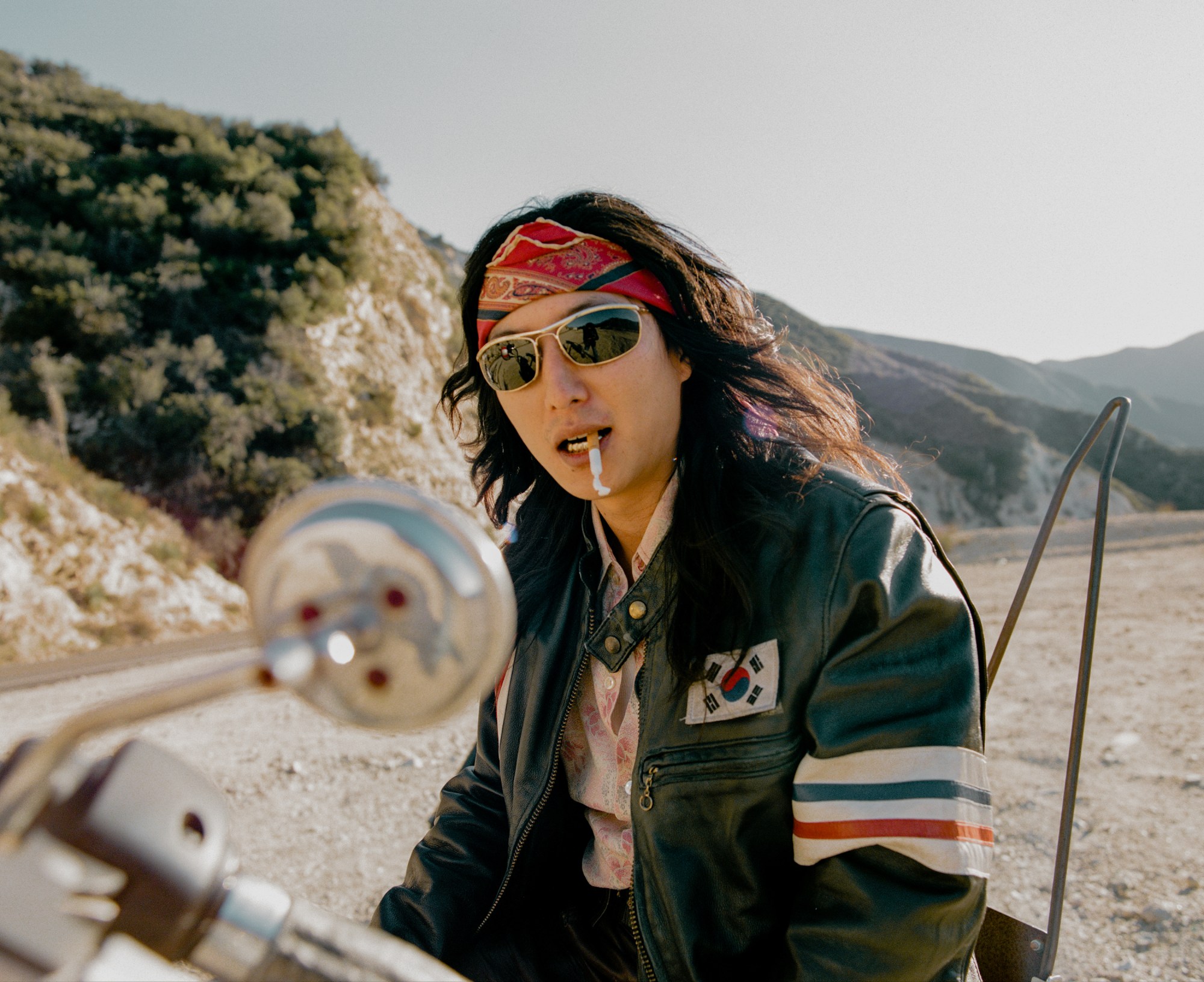 a man in a leather motorcycle jacket with the south korean flag on it in the desert wearing sunglasses