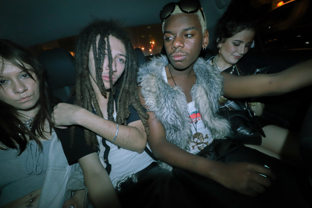 Four young people sit in the back of a cab; they look tired and a little worse for wear.