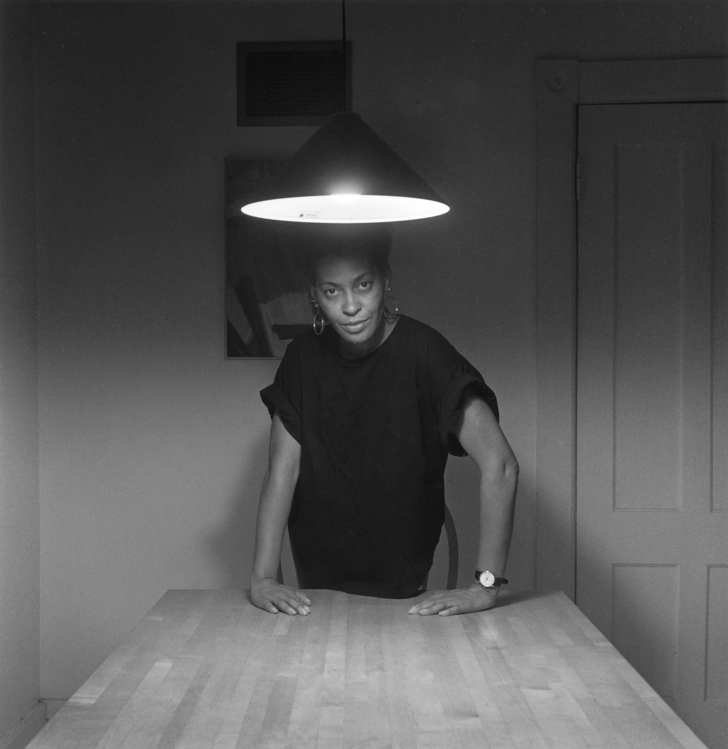 Carrie Mae Weems portrait standing at a table from kitchen table series