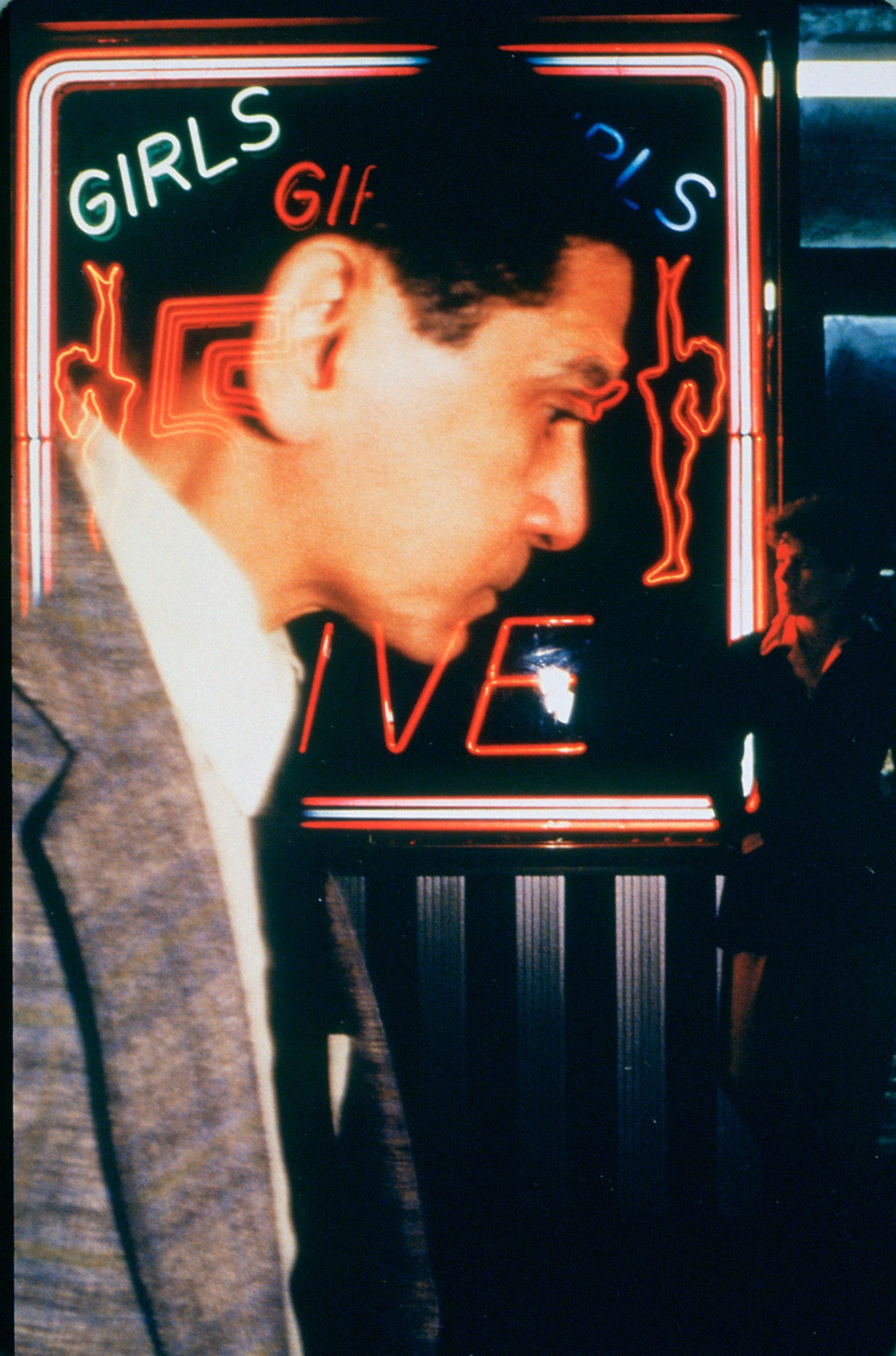 a man in a suit walking in front of a 'LIVE GIRLS' neon sign