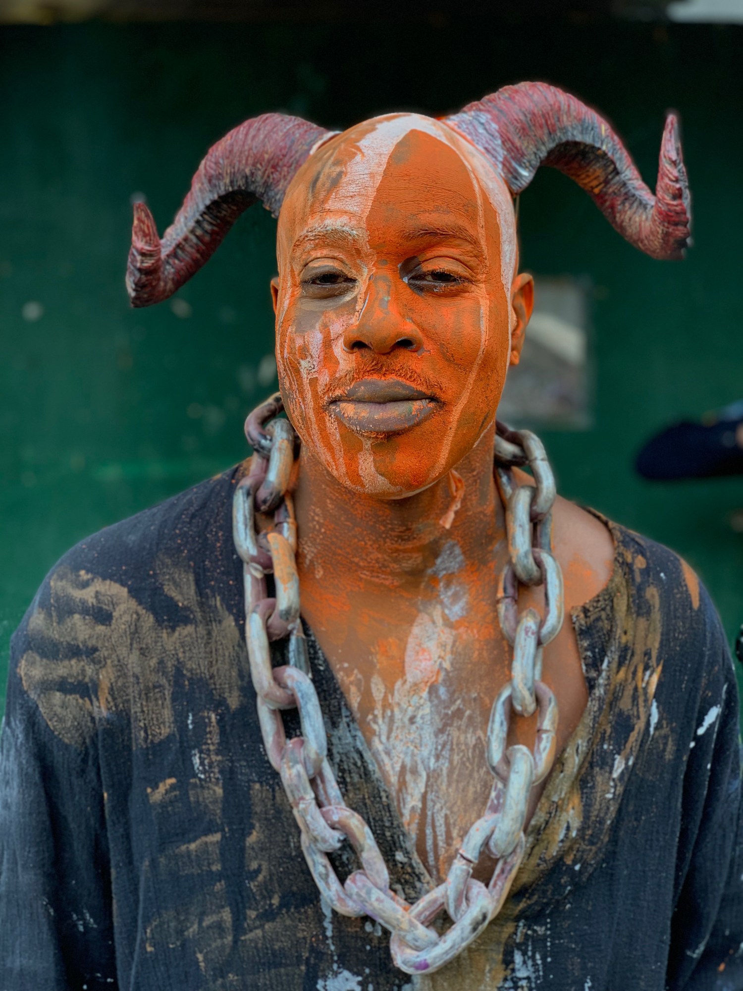 Photograph from End of the Line by Taylor Chapman of a man covered in orange paint wearing a chain around his neck and devil horns on his head