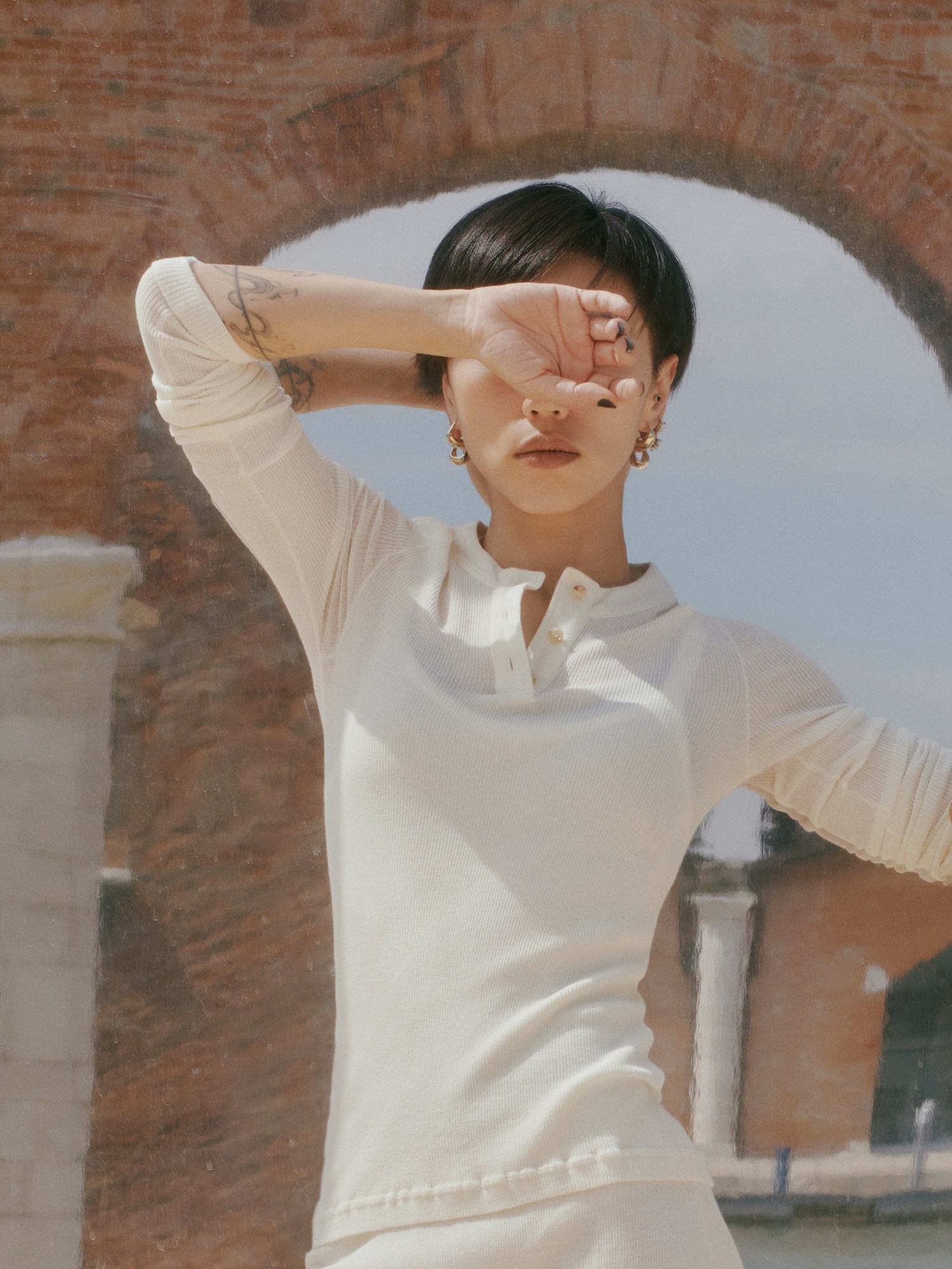 a portrait of the choreography xie xin wearing a white t-shirt covering her eyes