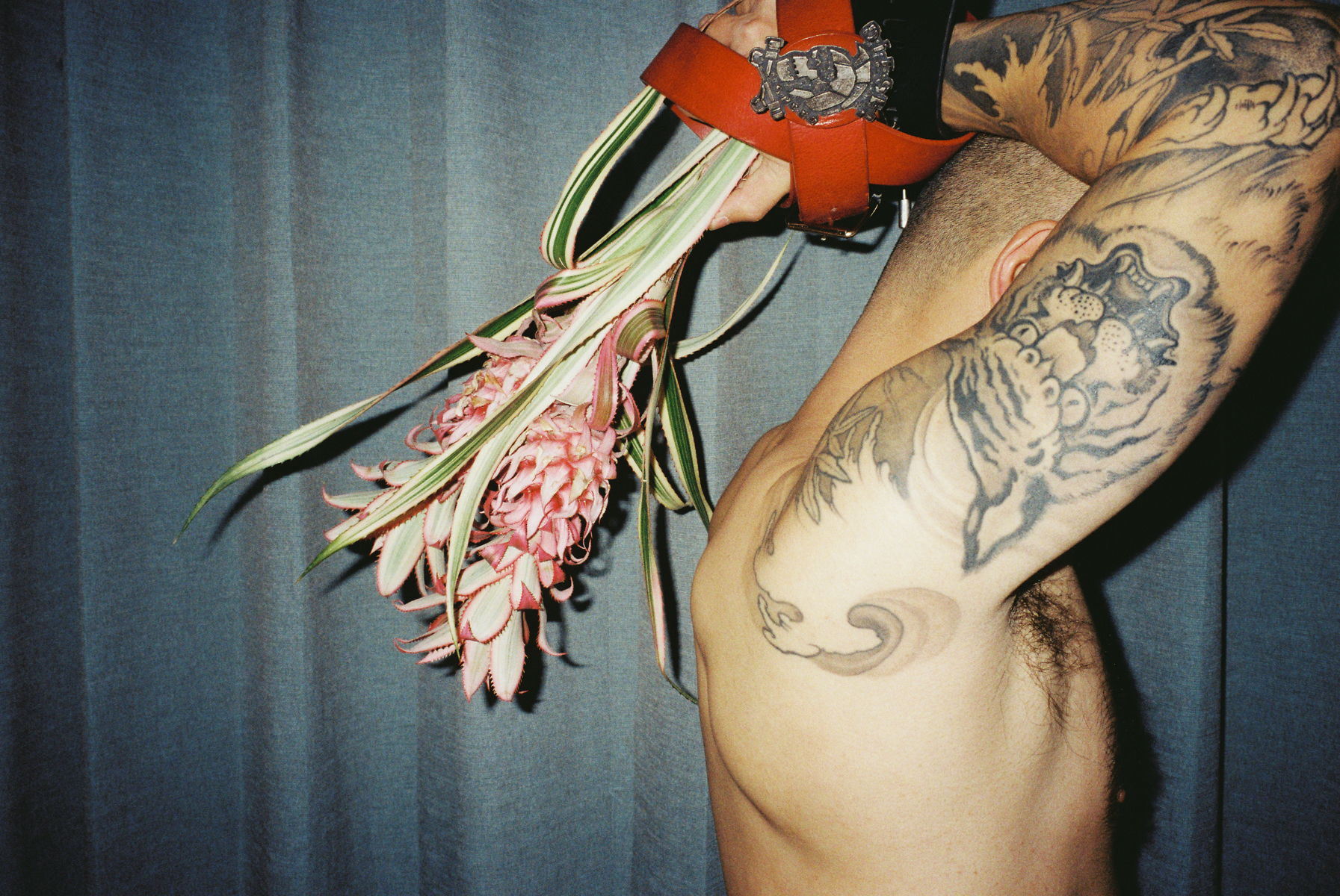 lin zhipeng photograph of tattooed chinese man with his hands about his head, holding a flower backwards behind his head.