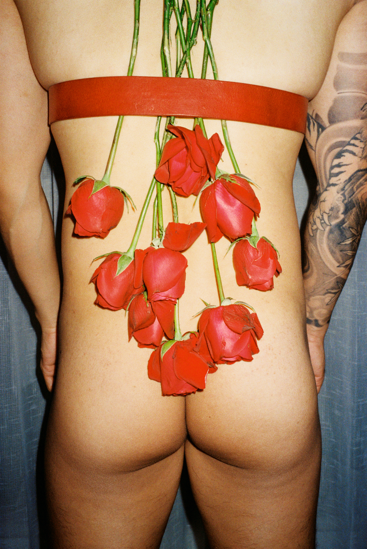 lin zhipeng photograph of a man nude from behind with roses strapped upside down to his back. you can see his buttocks.