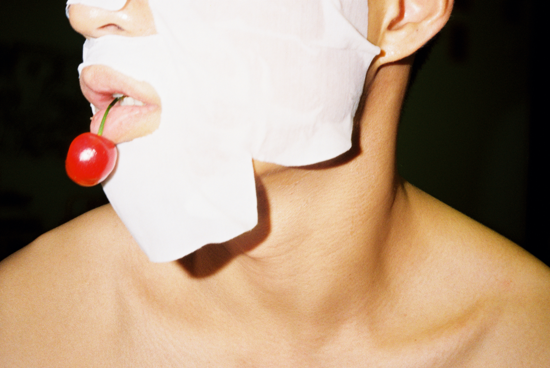 lin zhipeng photograph of a man in a face sheet mask with a cherry in his mouth.