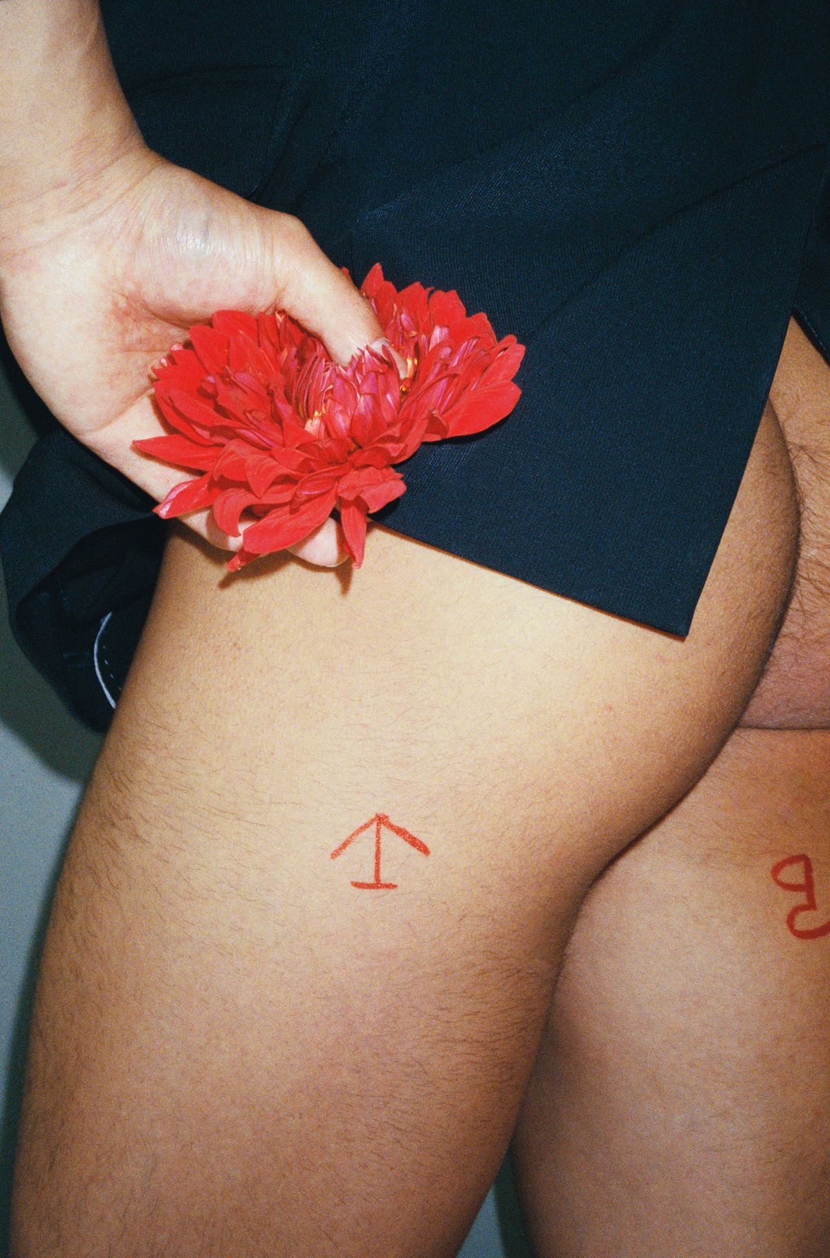 lin zhipeng photograph of a man from behind naked, he has pen marks on his upper thighs and a flower is being handed to him.