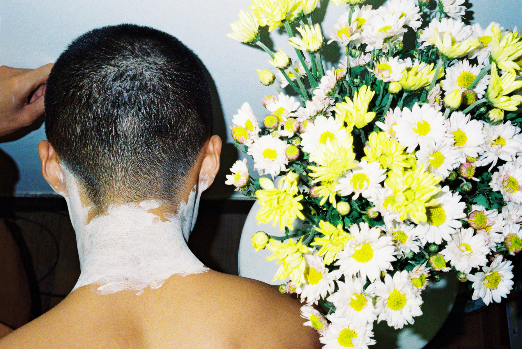 lin zhipeng photograph of. man from behind with sunblock on his neck. a bunch of daisies are in front of him.