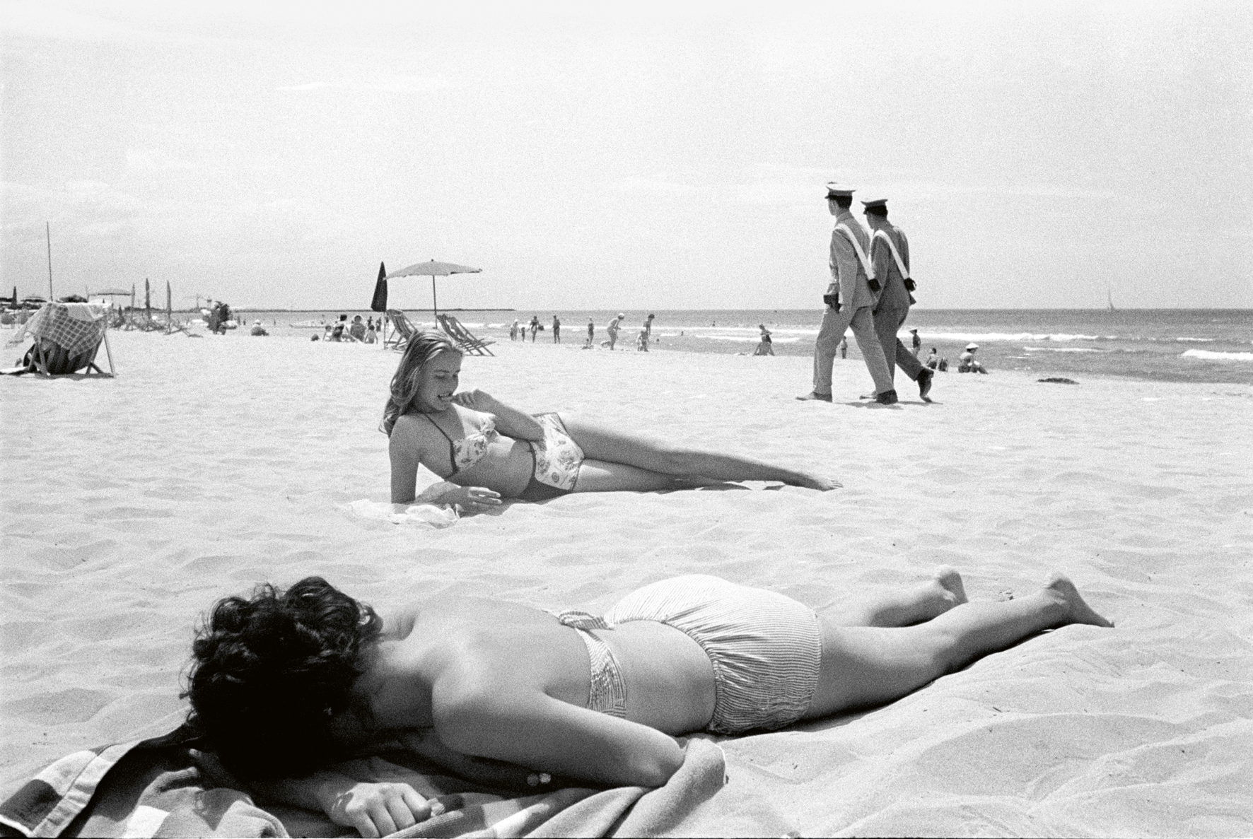 a black and white photograph by paolo di paolo of two women sunbathing on a beach in tuscany.