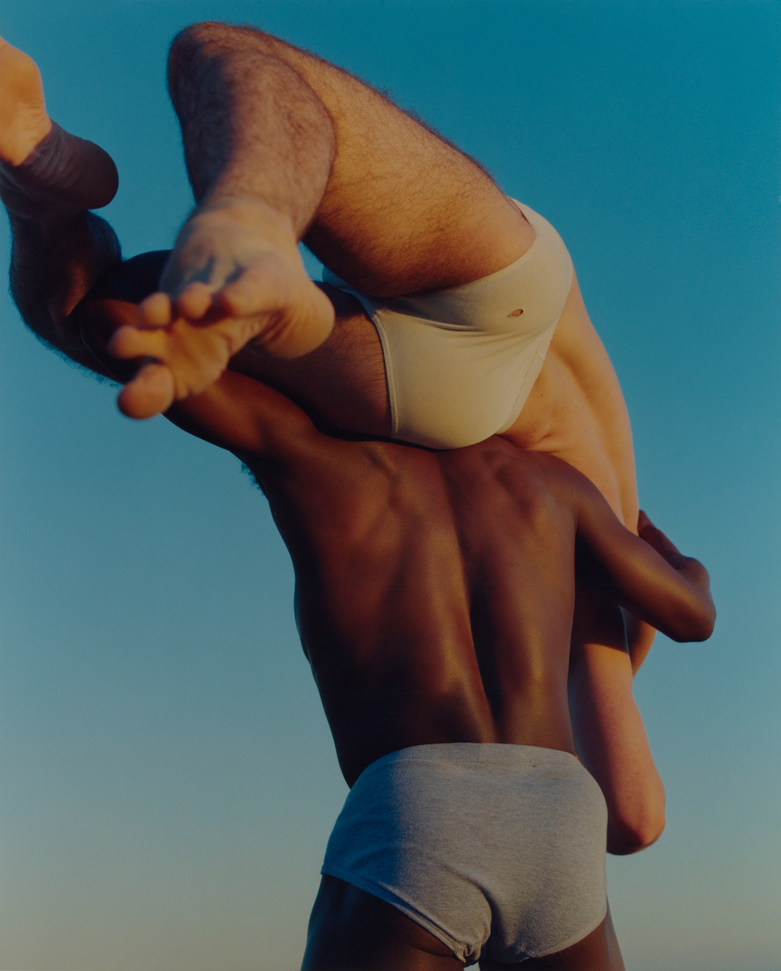 two men in underwear wrestling against a blue background