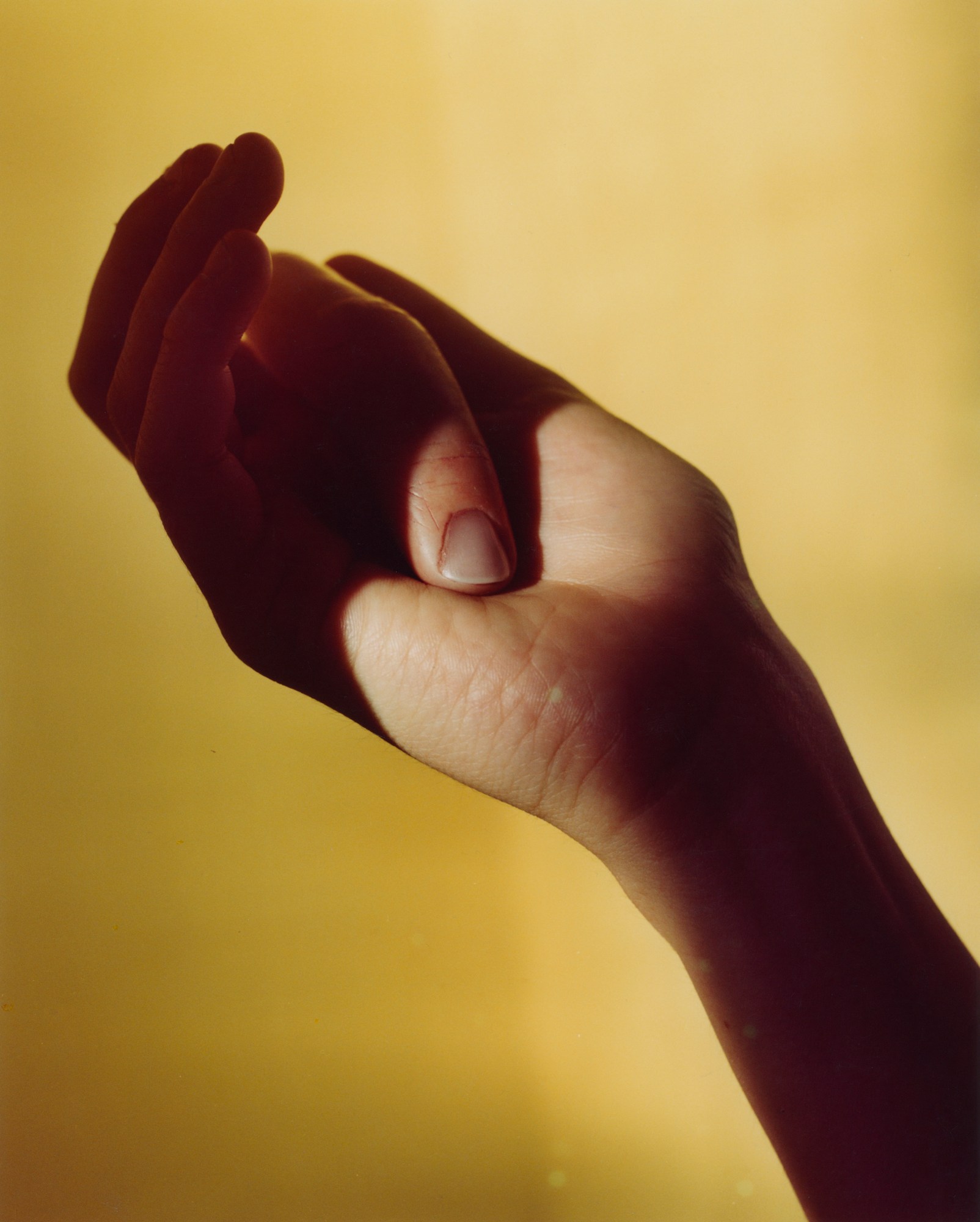 a hand holding a finger in the palm, against a yellow background