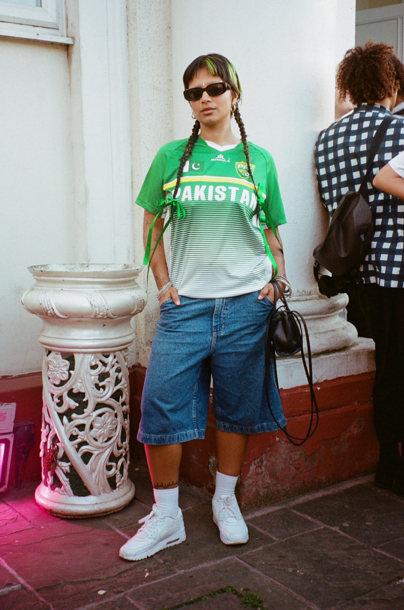 a young south asian woman with green bits in her hair wears a pakistan football shirt