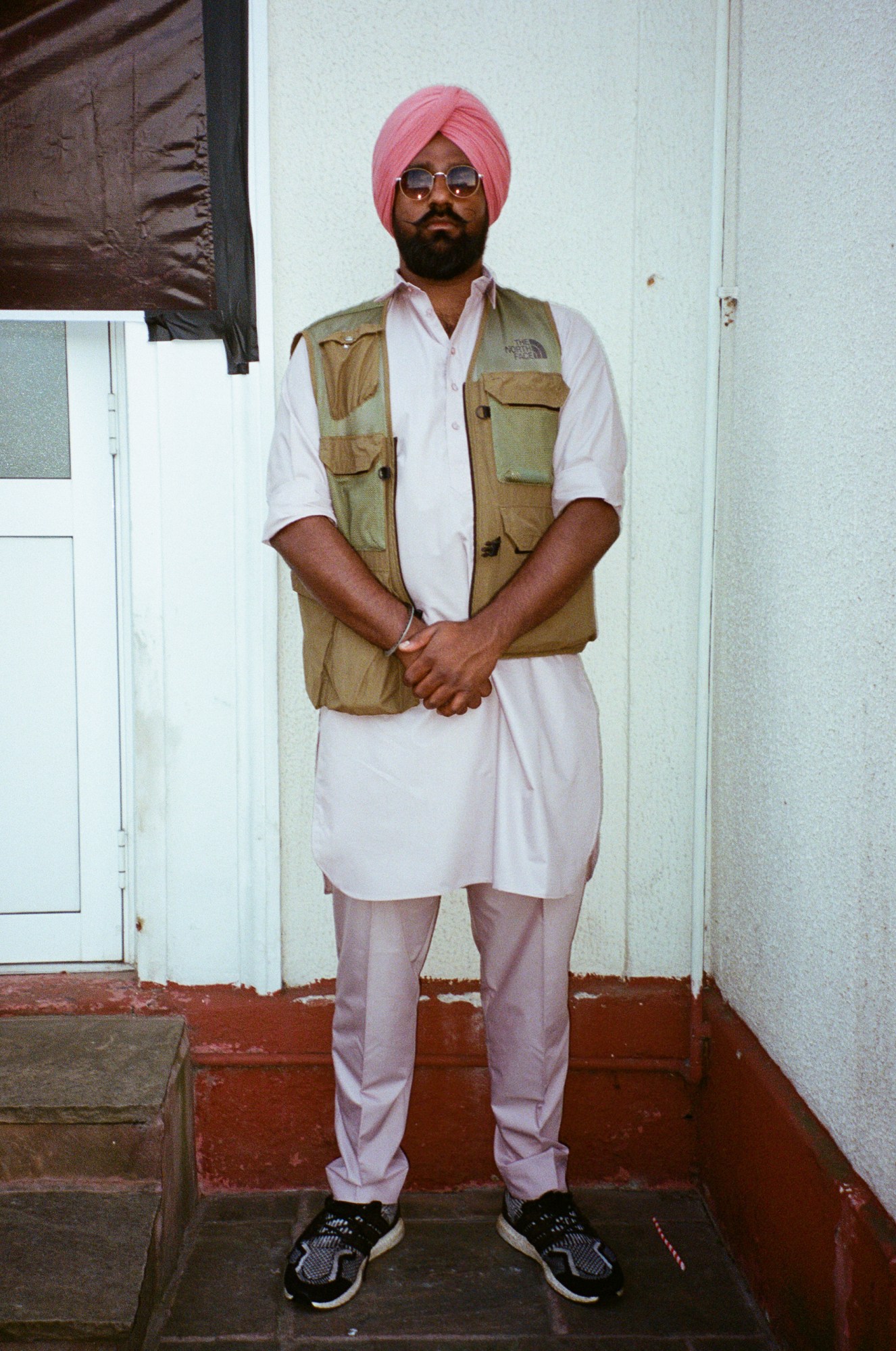 a sikh man in a pink turban wears a north face gilet over a pale pink outfit