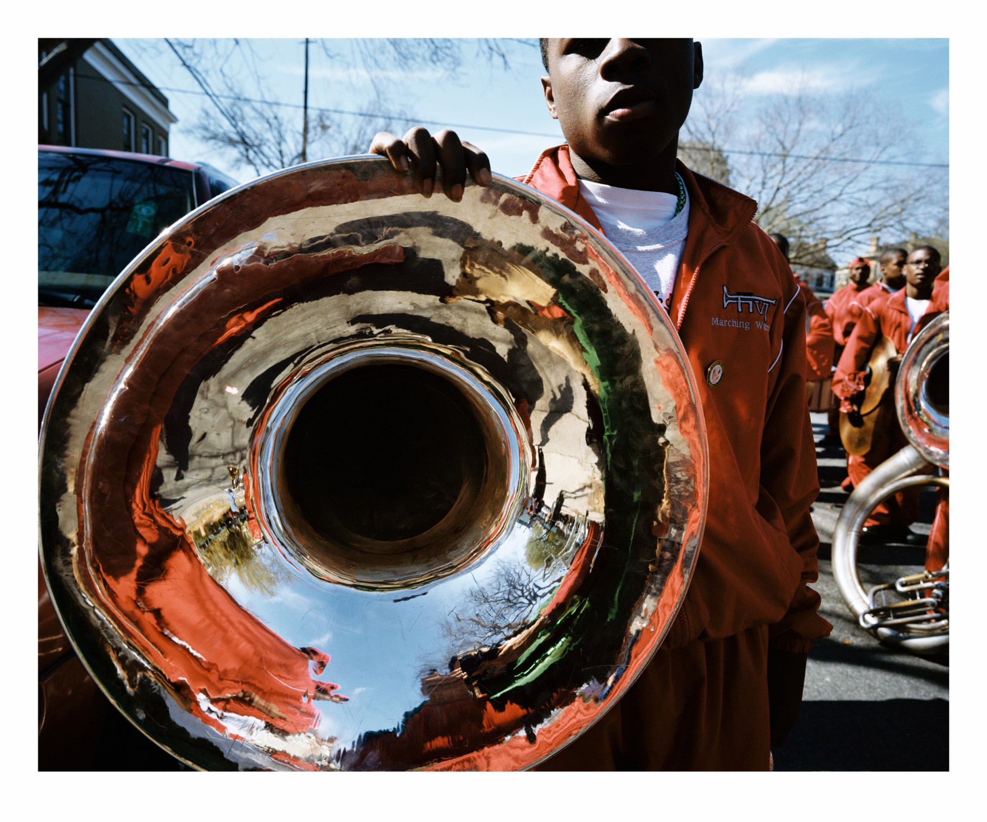 a man holds a tuba wearing an orange band tracksuit