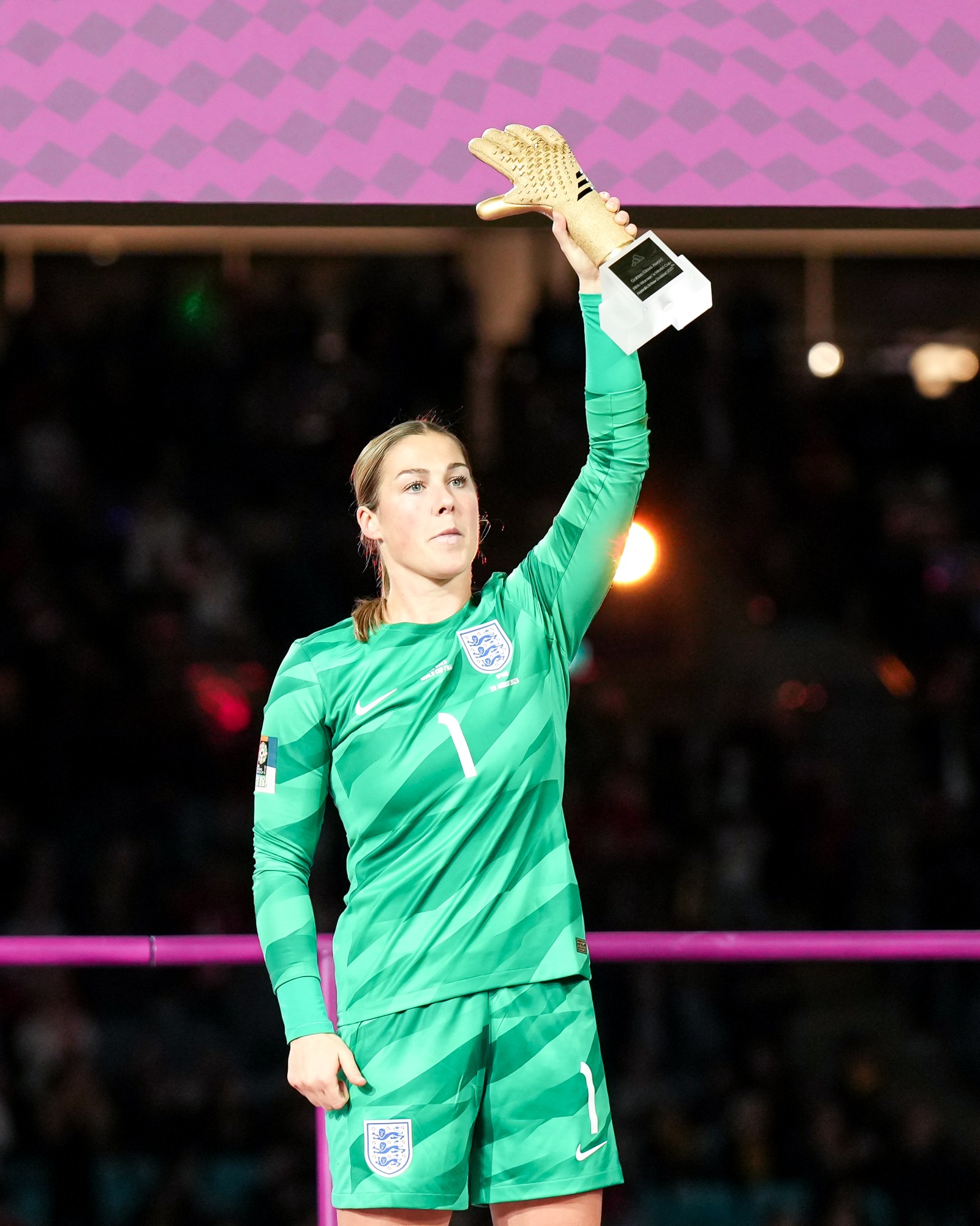 female soccer player in green uniform holding trophy