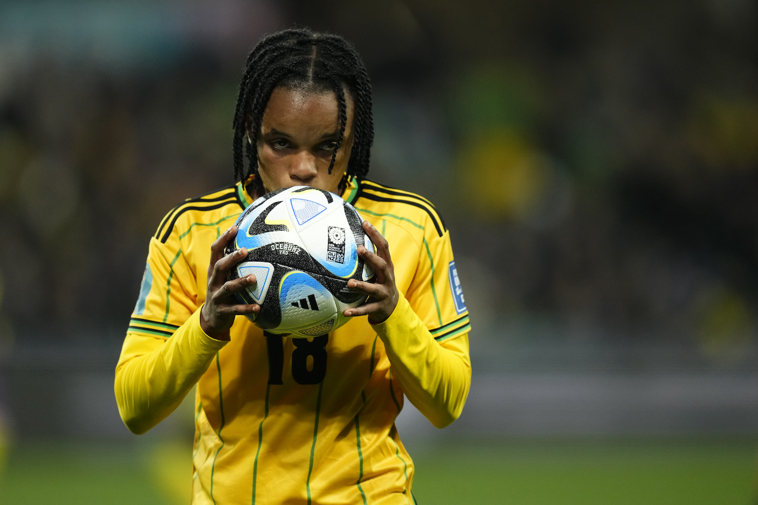 female football player in yellow jersey holding a black and blue ball