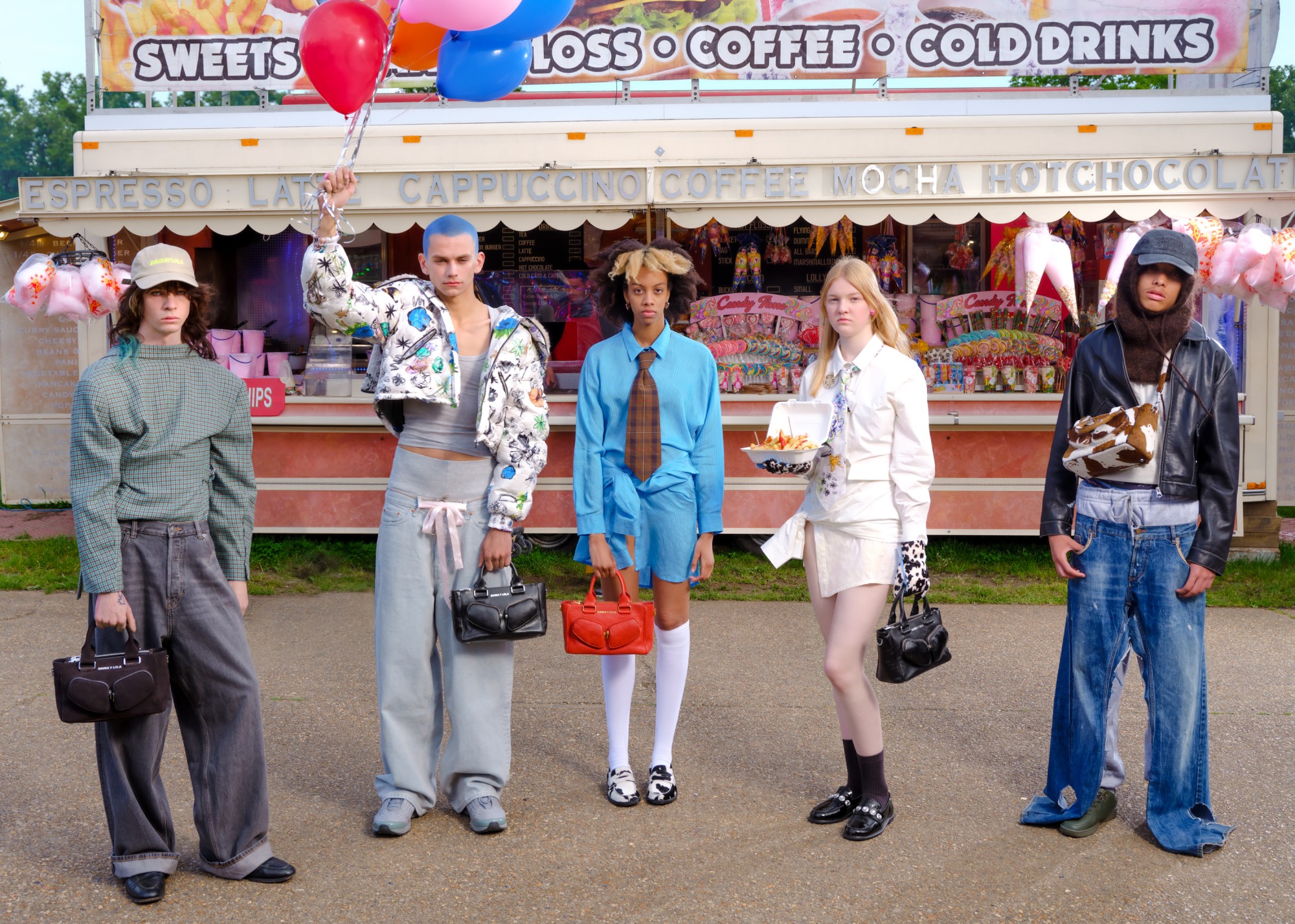 five models stand in a line in front of a sweet stall; they hold colourful balloons, leather handbags and an open box of chips