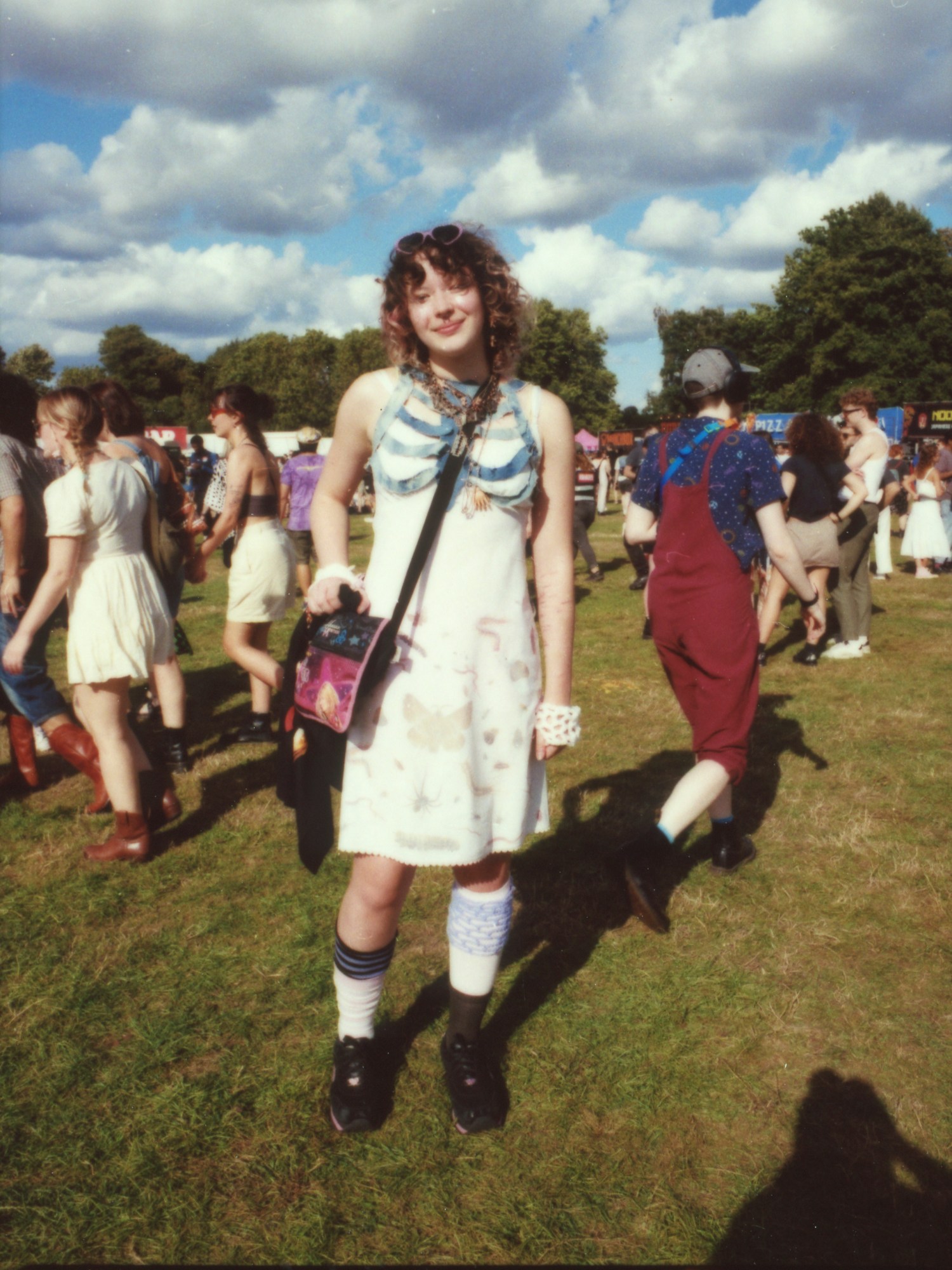 a girl with curly hair and a pretty dress covered in bugs smiles; she has a handmade denim ribcage worn over the dress photographed by Jody Evans