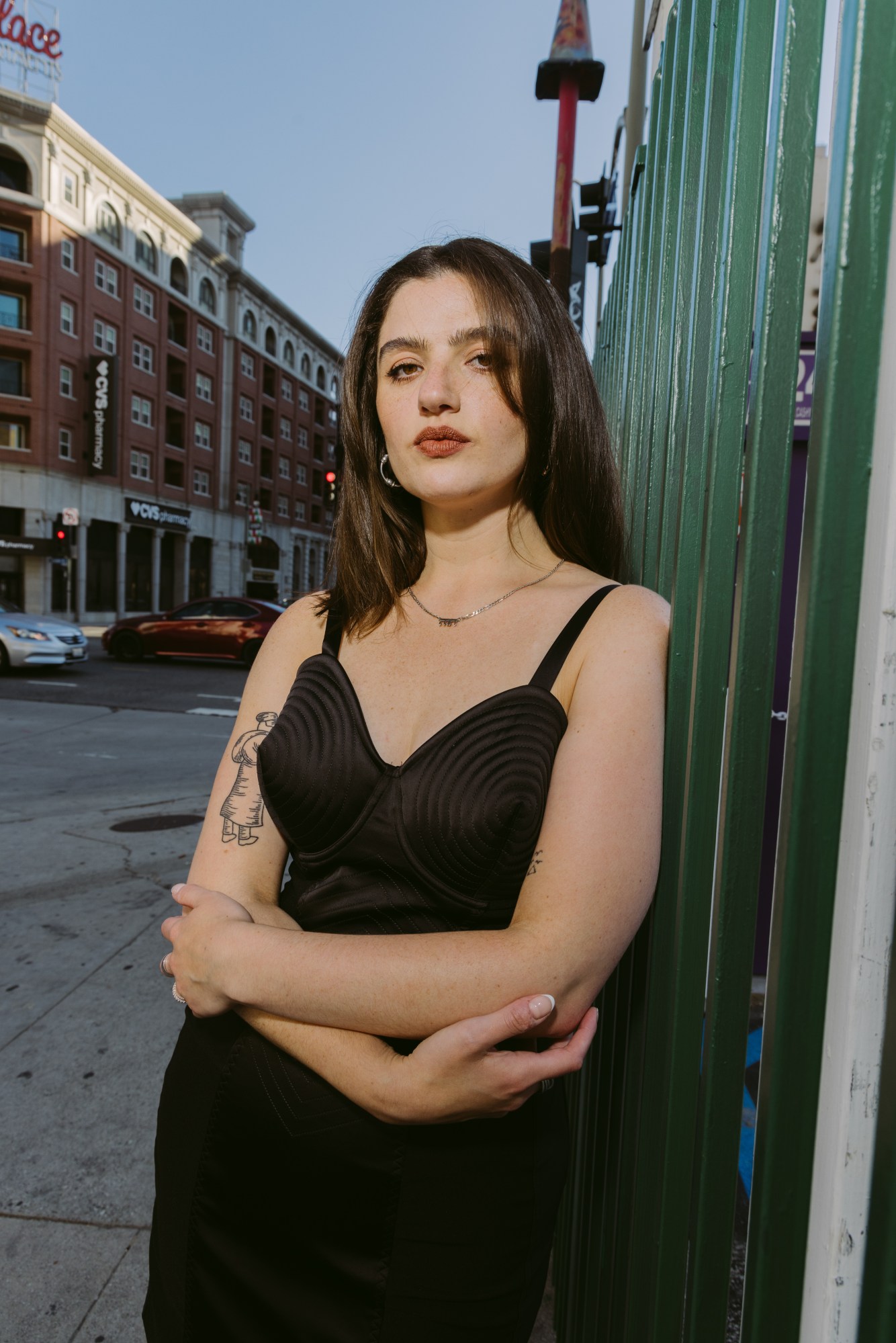 the director emma seligman standing in a new york street in a black dress, her arms crossed gently in front of her