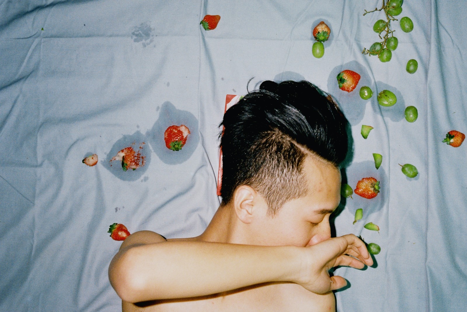 a young man on blue sheets covered in smashed fruit