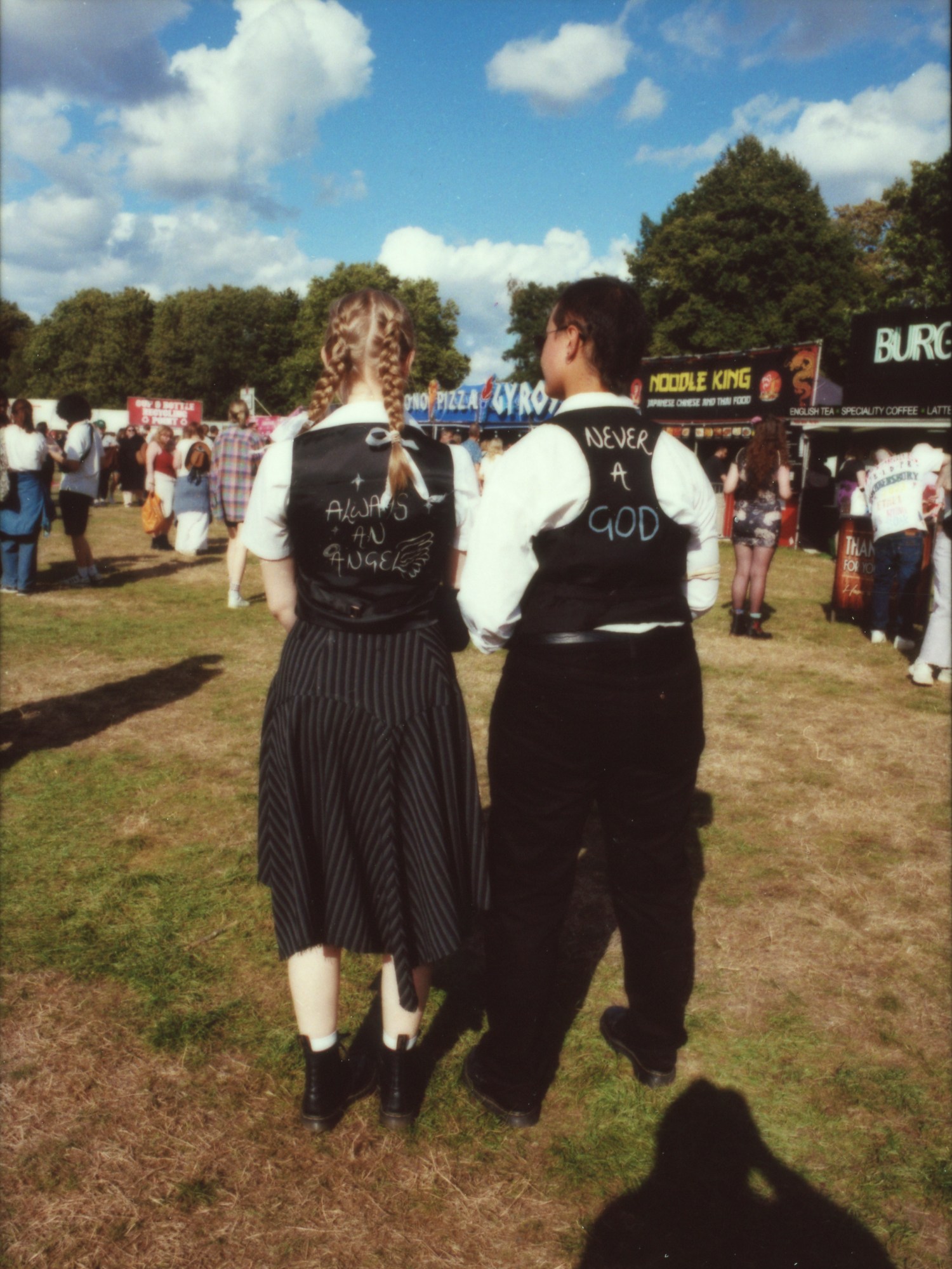 the backs of two people wearing matching vests over shirts; they have handwritten the lyrics always an angel and never a god on the backs photographed by Jody Evans