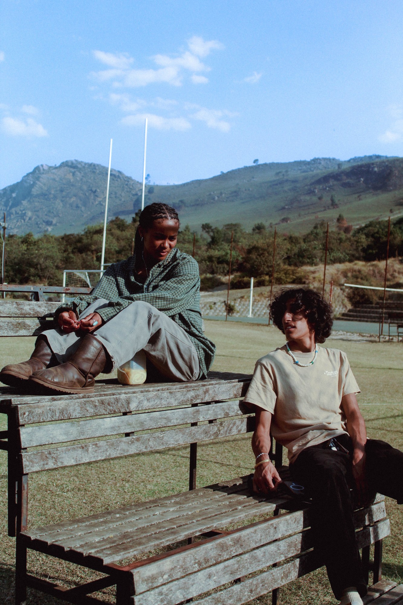 two teenagers talking on a wooden bench in a field