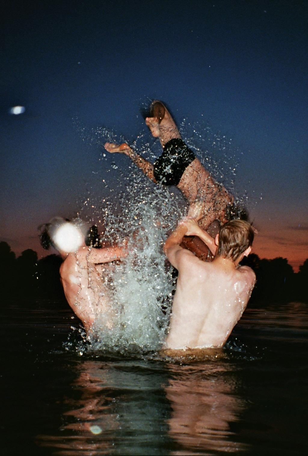 three teenagers splashing in the river at nighttime