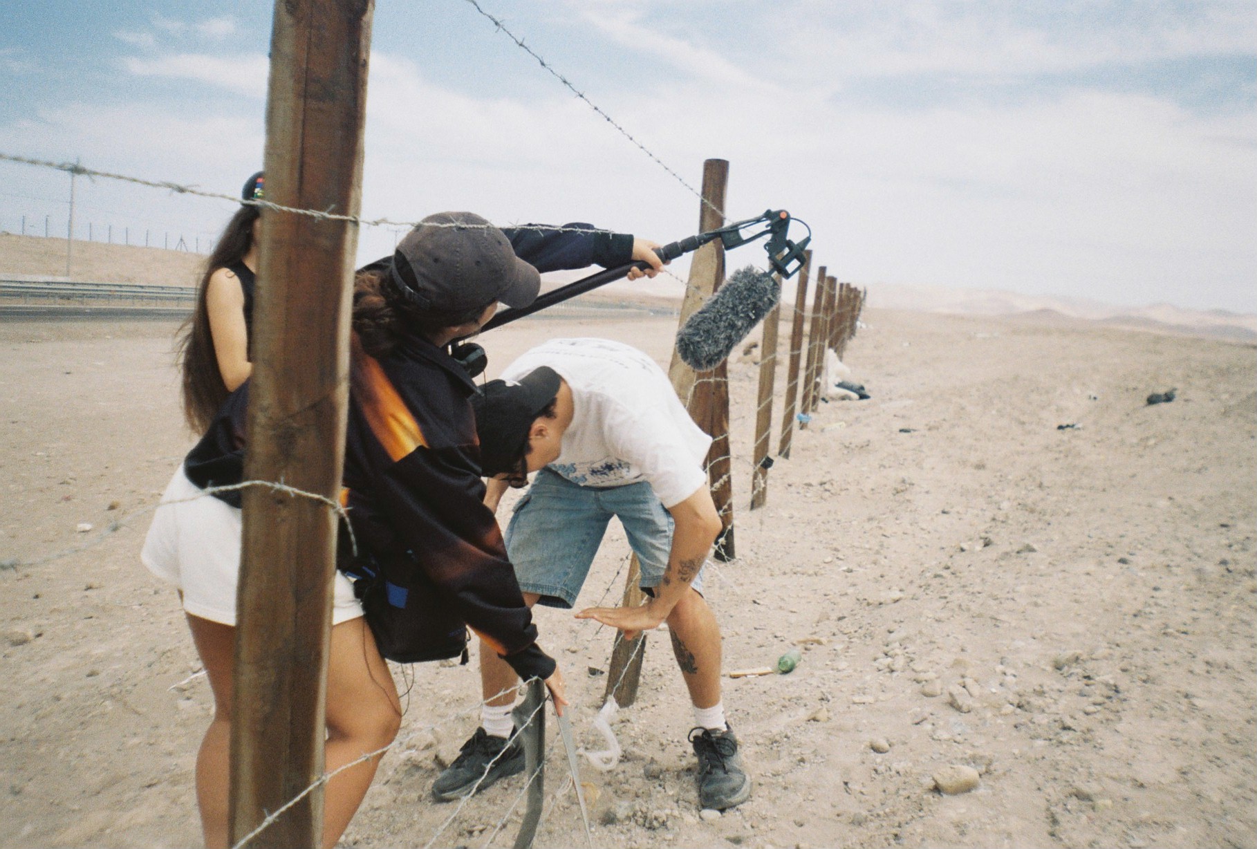 three people sneaking through a barbed wire fence in the desert