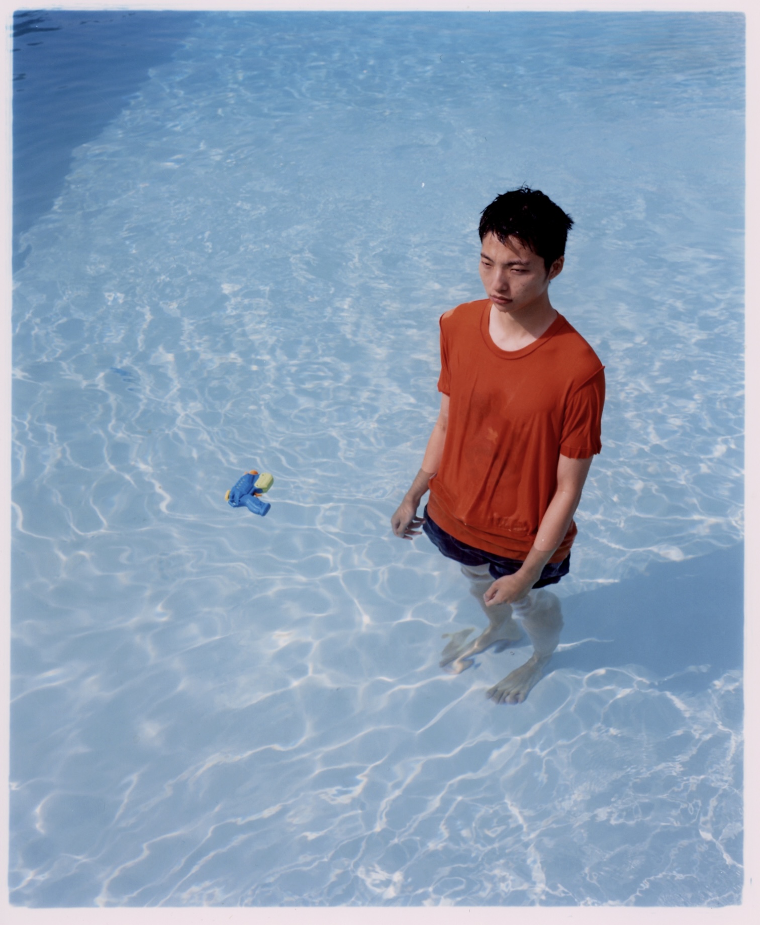 a young man in a red shirt standing in a pool next to a water gun