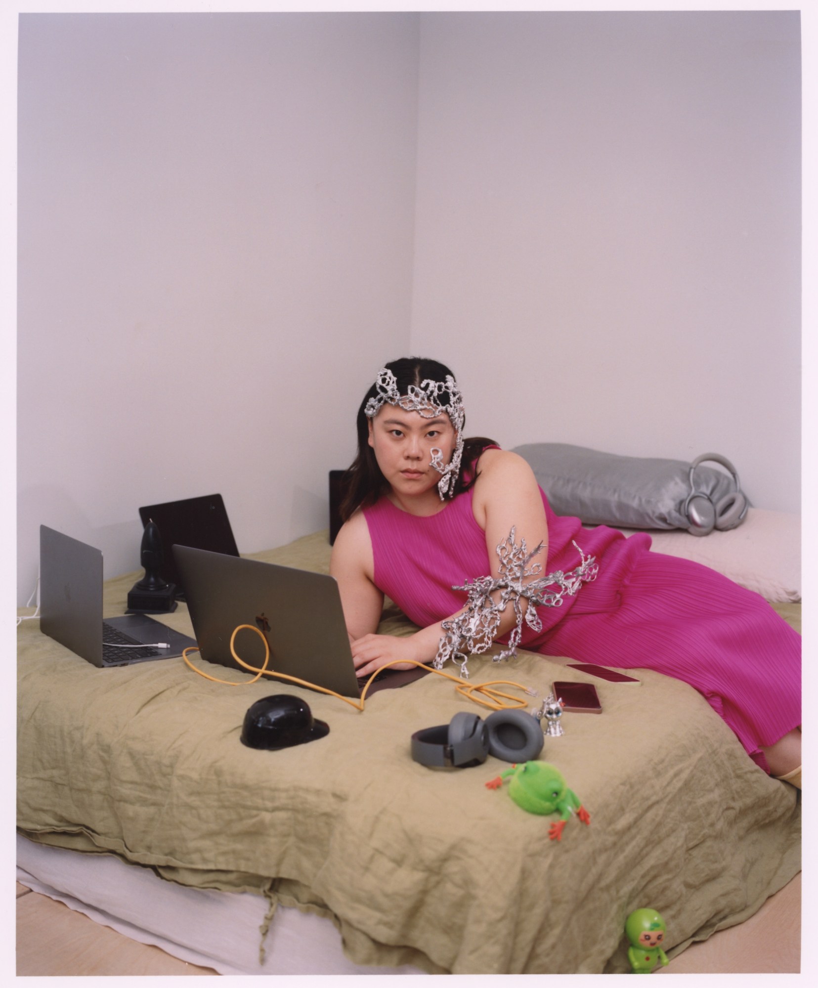 a woman in a pink dress wearing silver sculptural jewelry surrounded by multiple laptops and other electronics