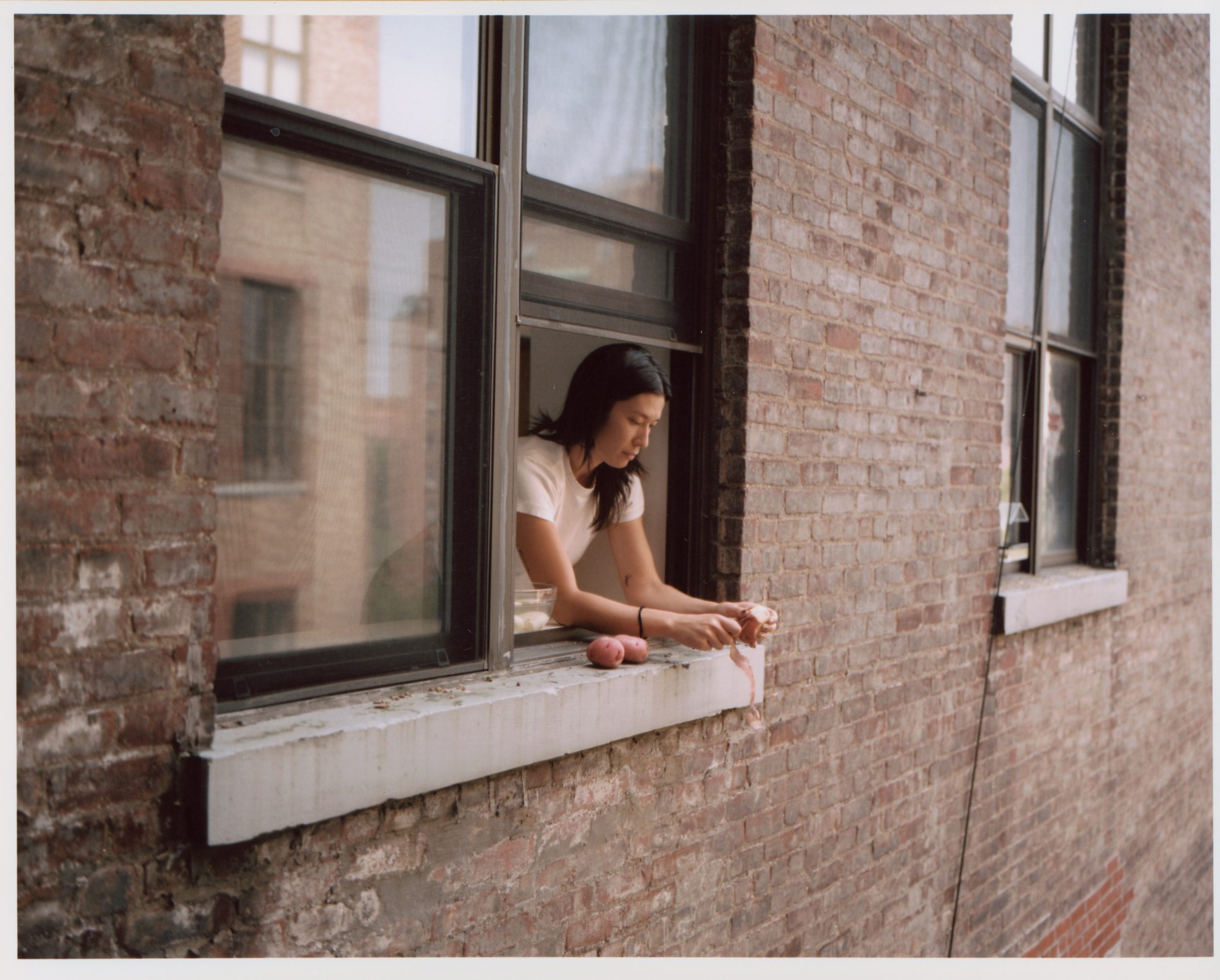 a young woman peeling a potato near an open window