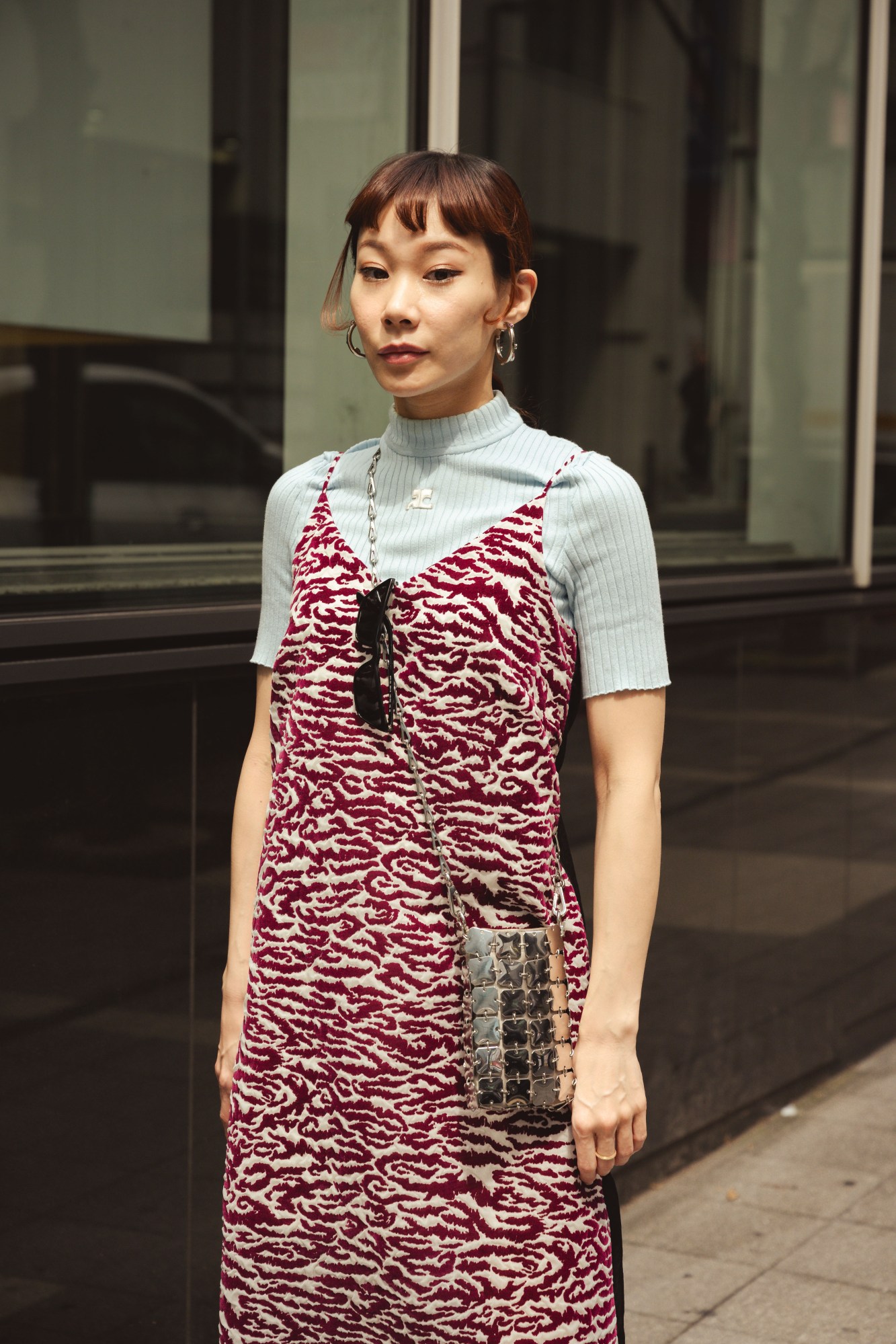 a japanese woman wears a red and white patterned dress over a ribbed top. she has a baby fringe and silver hoop earrings in