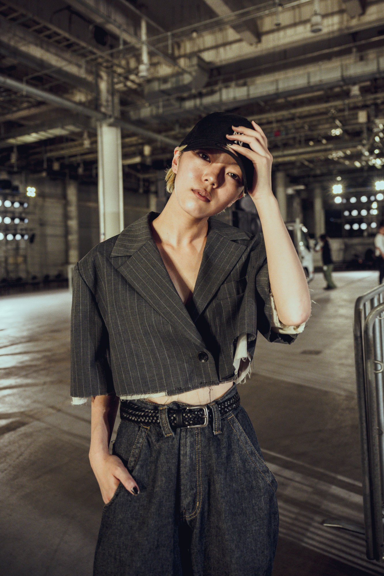 a young androgynous model with cropped bleach blonde hair wears dark denim jeans with a cut-off pin-stripe suit jacket