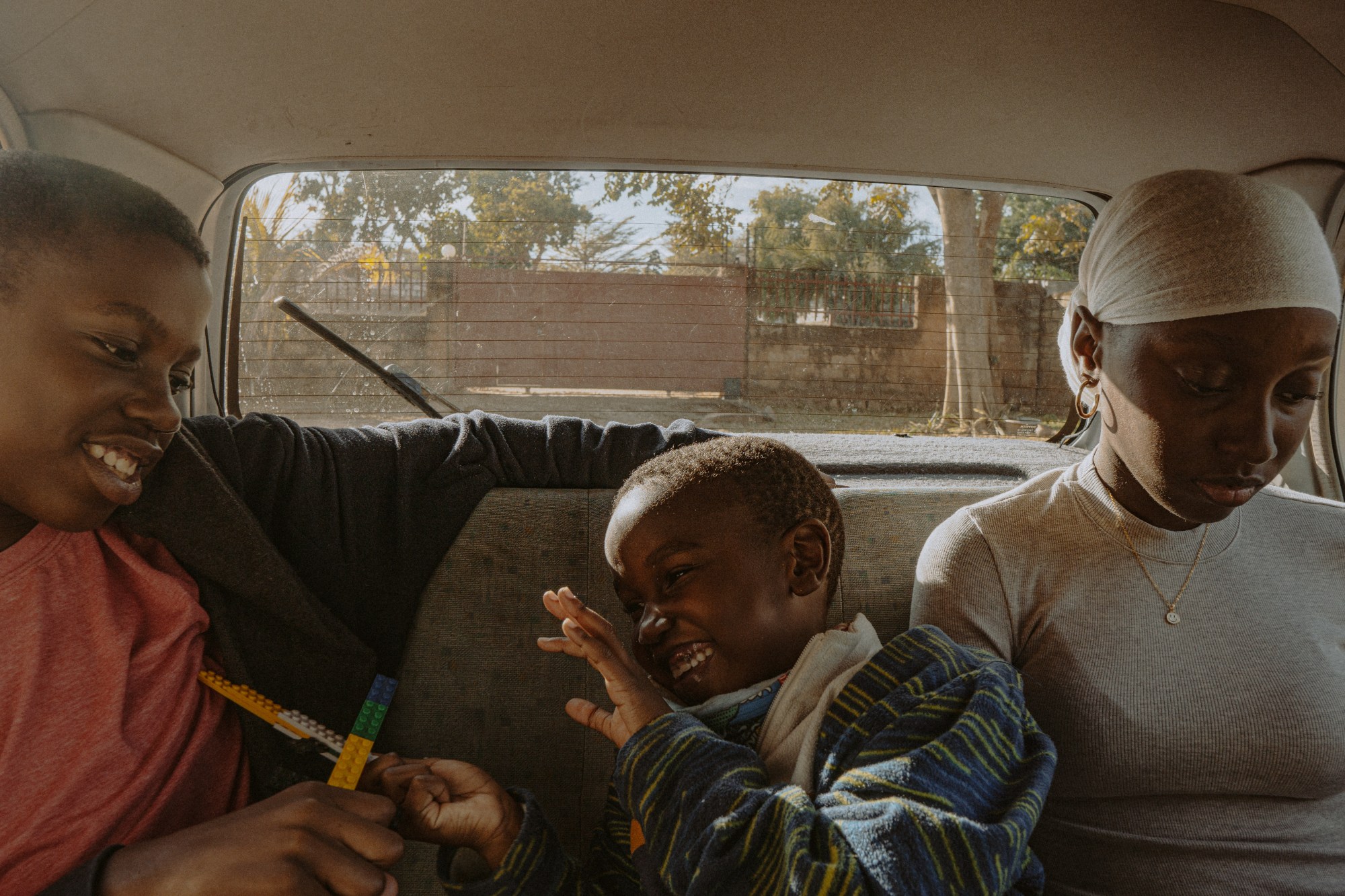 two boys and a girl in the backseat of their car with the sun shining through the window