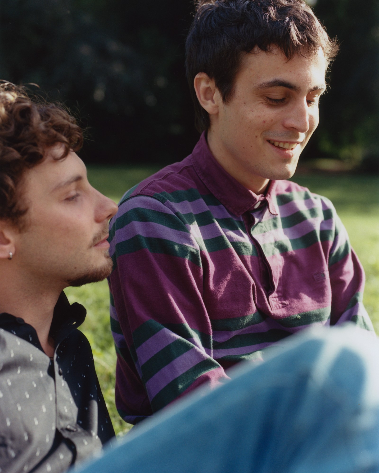 'lie with me' actors Jérémy Gillet and Julien De Saint Jean smiling next to each other as they sit in a park