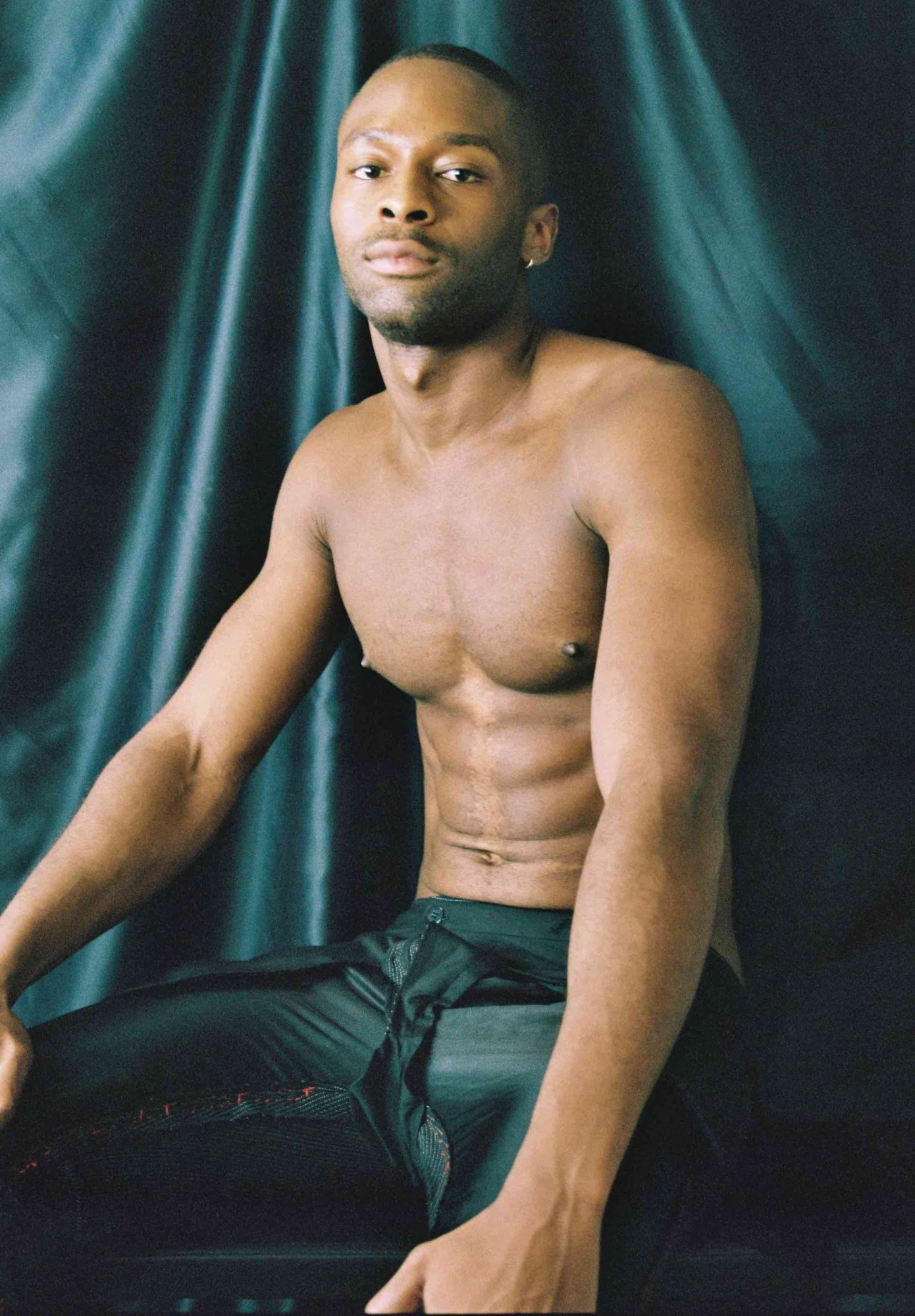 a young man in black pants posing shirtless in front of a black backdrop