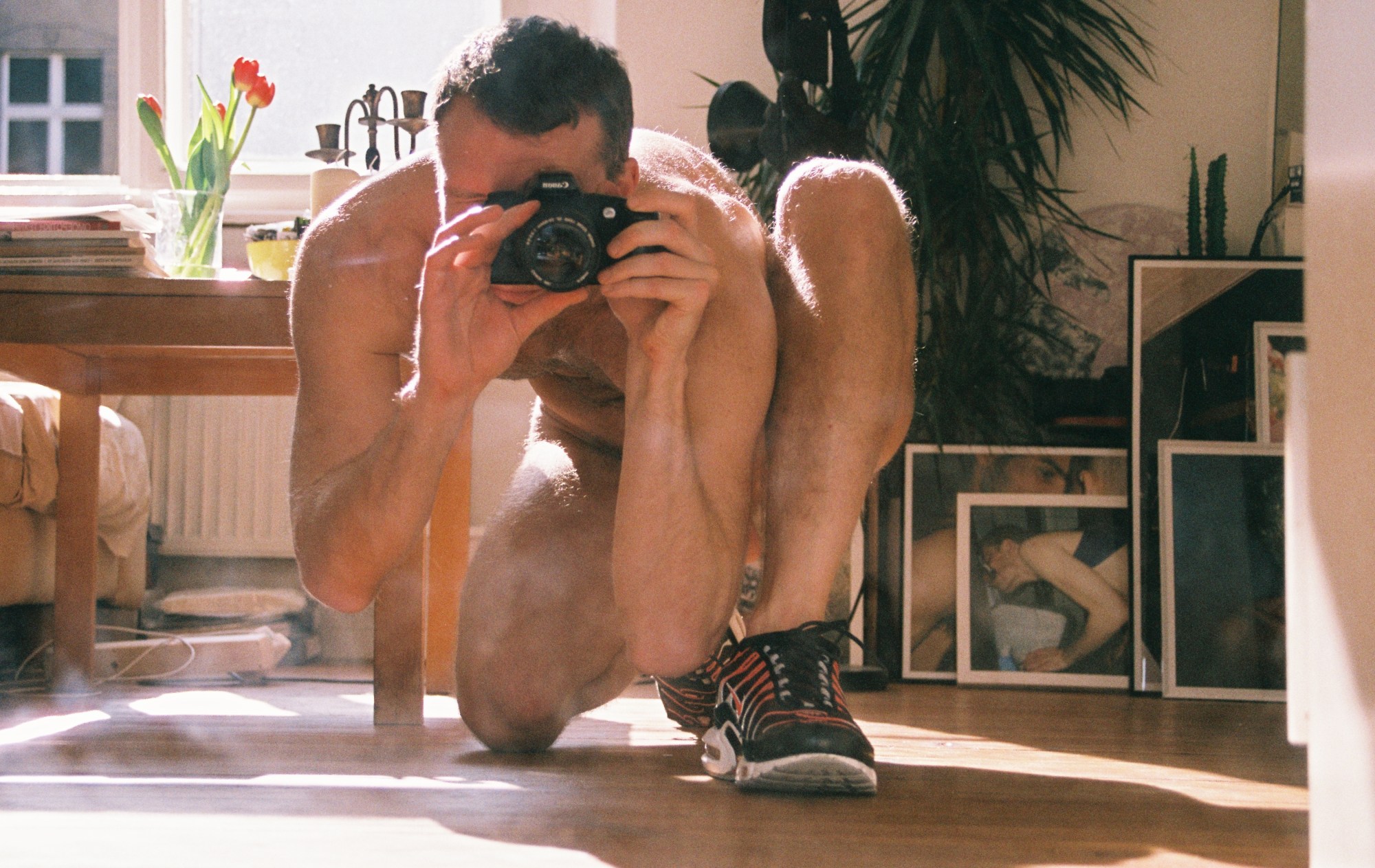 a photographer taking a self portrait in an apartment while nude and wearing sneakers