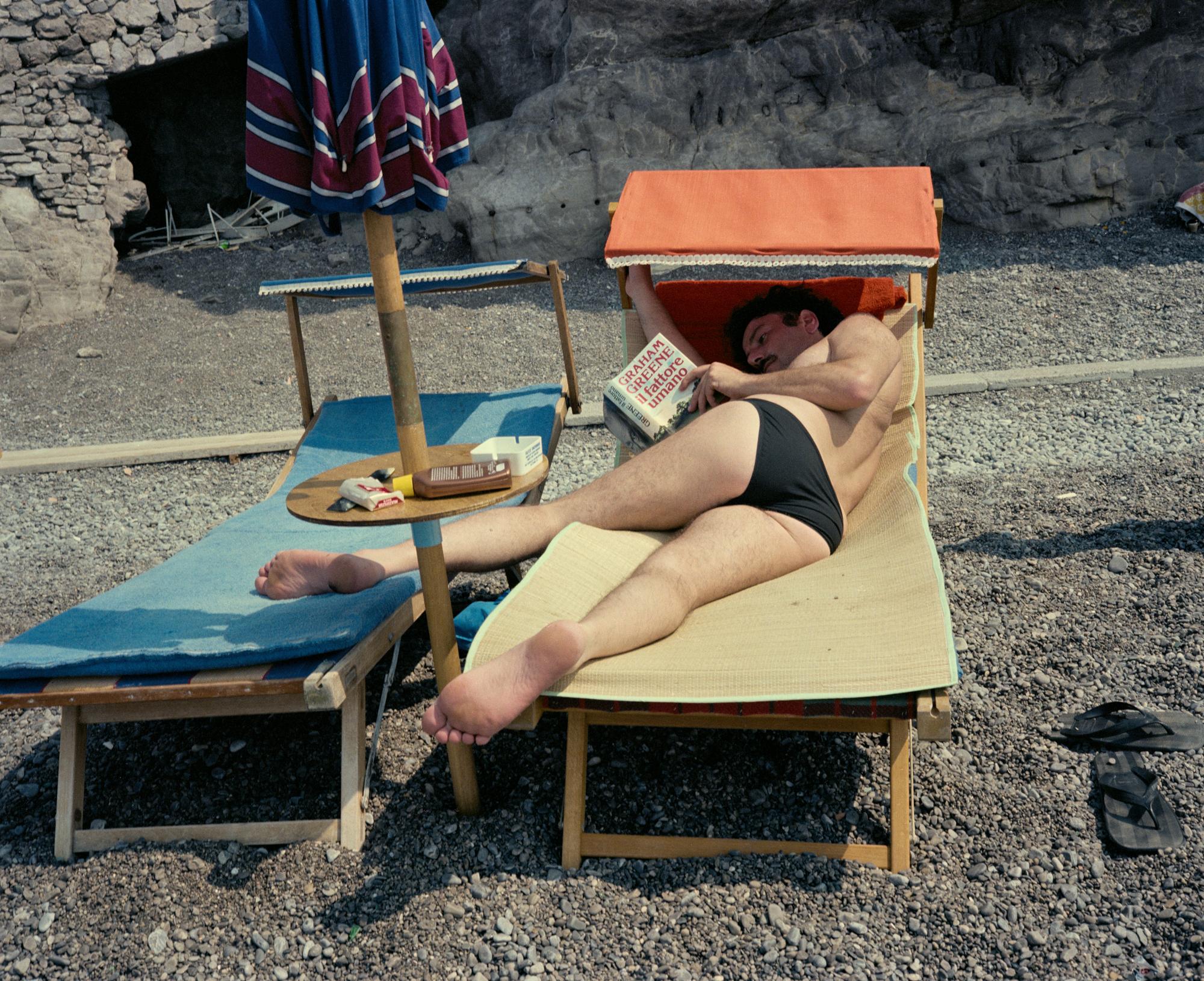 under a canopy, a man reads a book on the beach