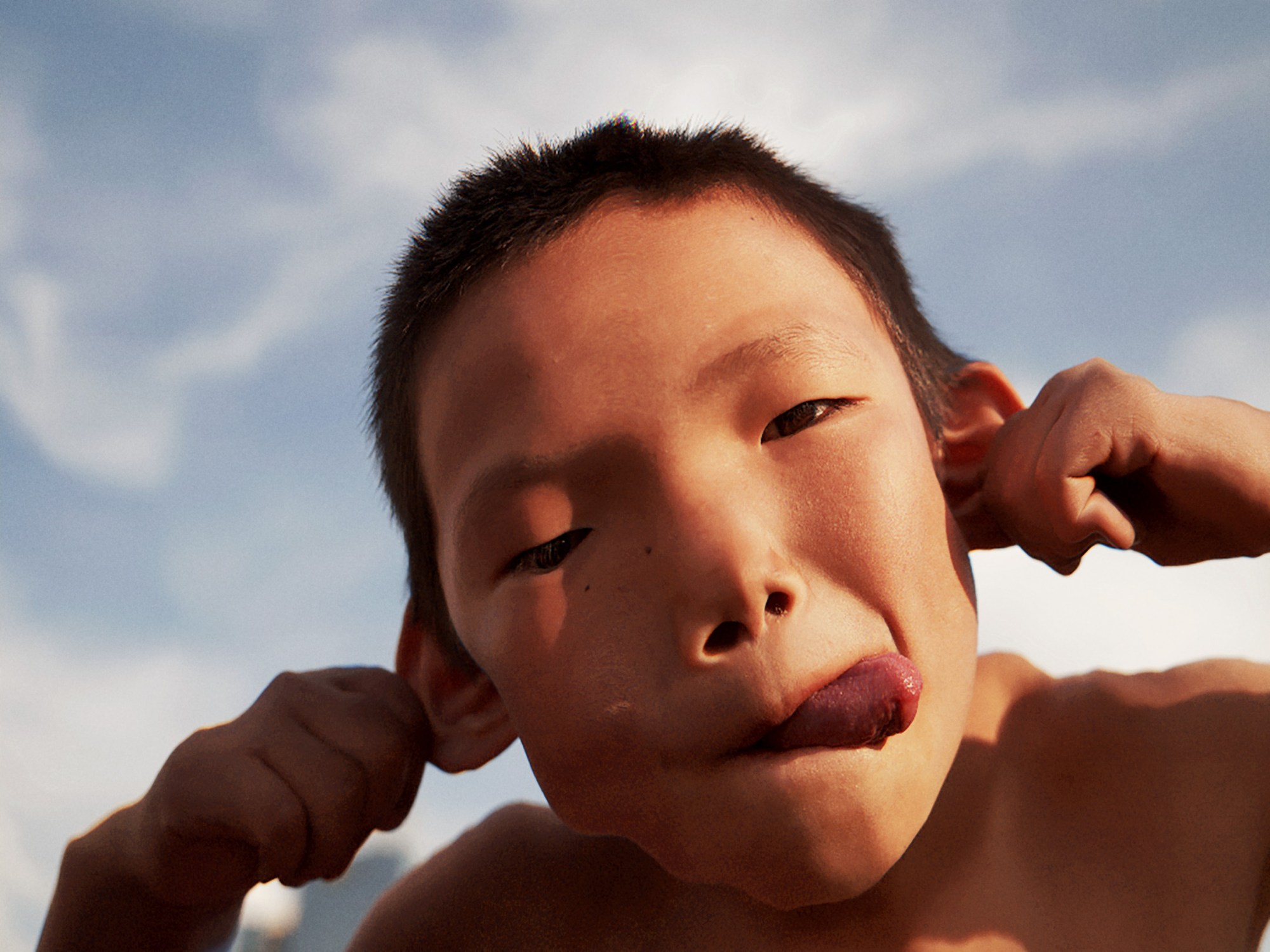 a young mongolian boy sticks out his tongue and holds his ears out