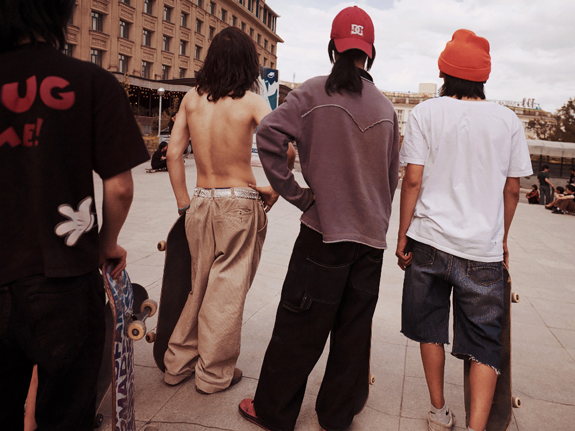 teen mongolian skaters stand in a city square watching their friends