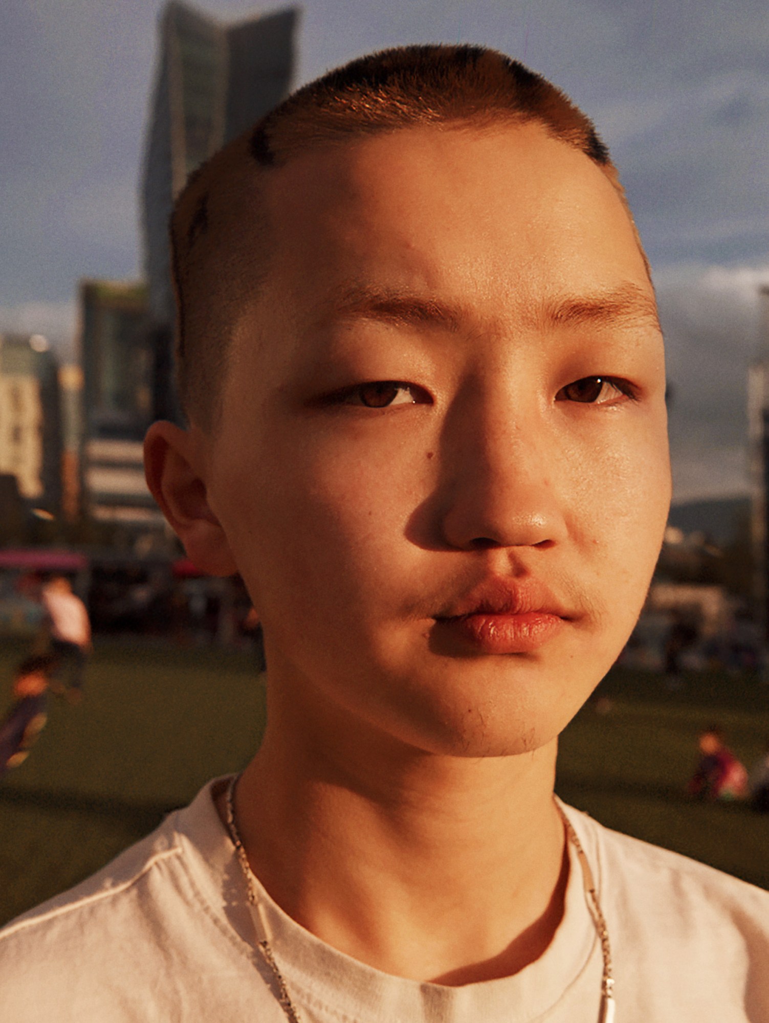 a mongolian teen with a buzzcut stands in golden hour light looking to camera