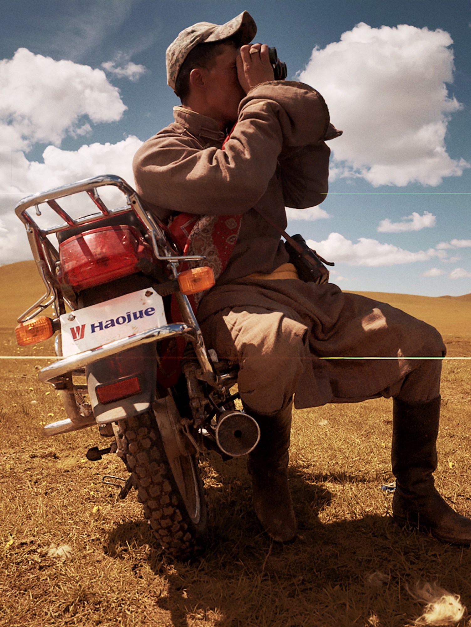 a man in a beige linen suit leans against his motorbike in the mongolian countryside