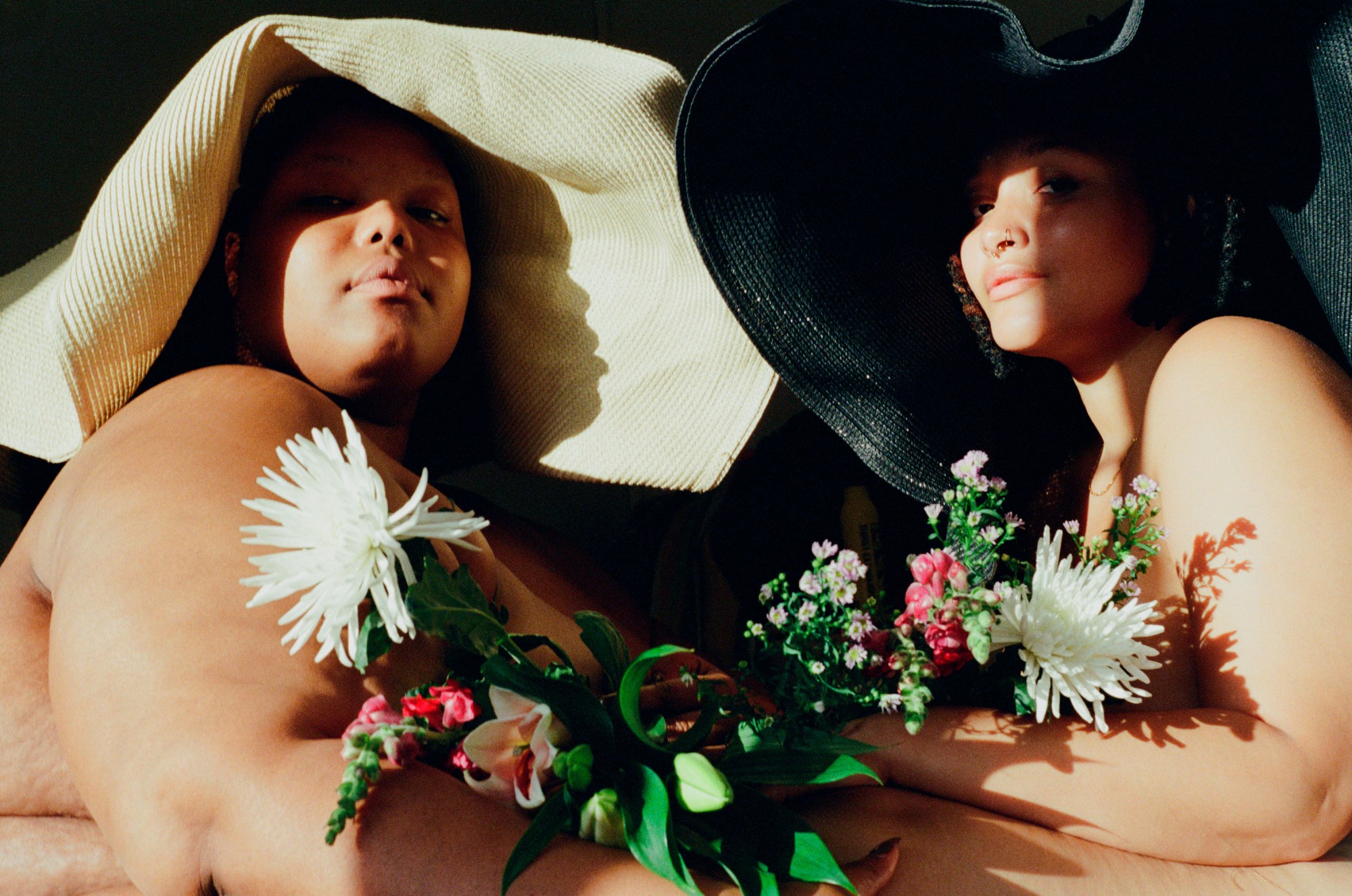 two women wearing large straw hats while holding bouqets