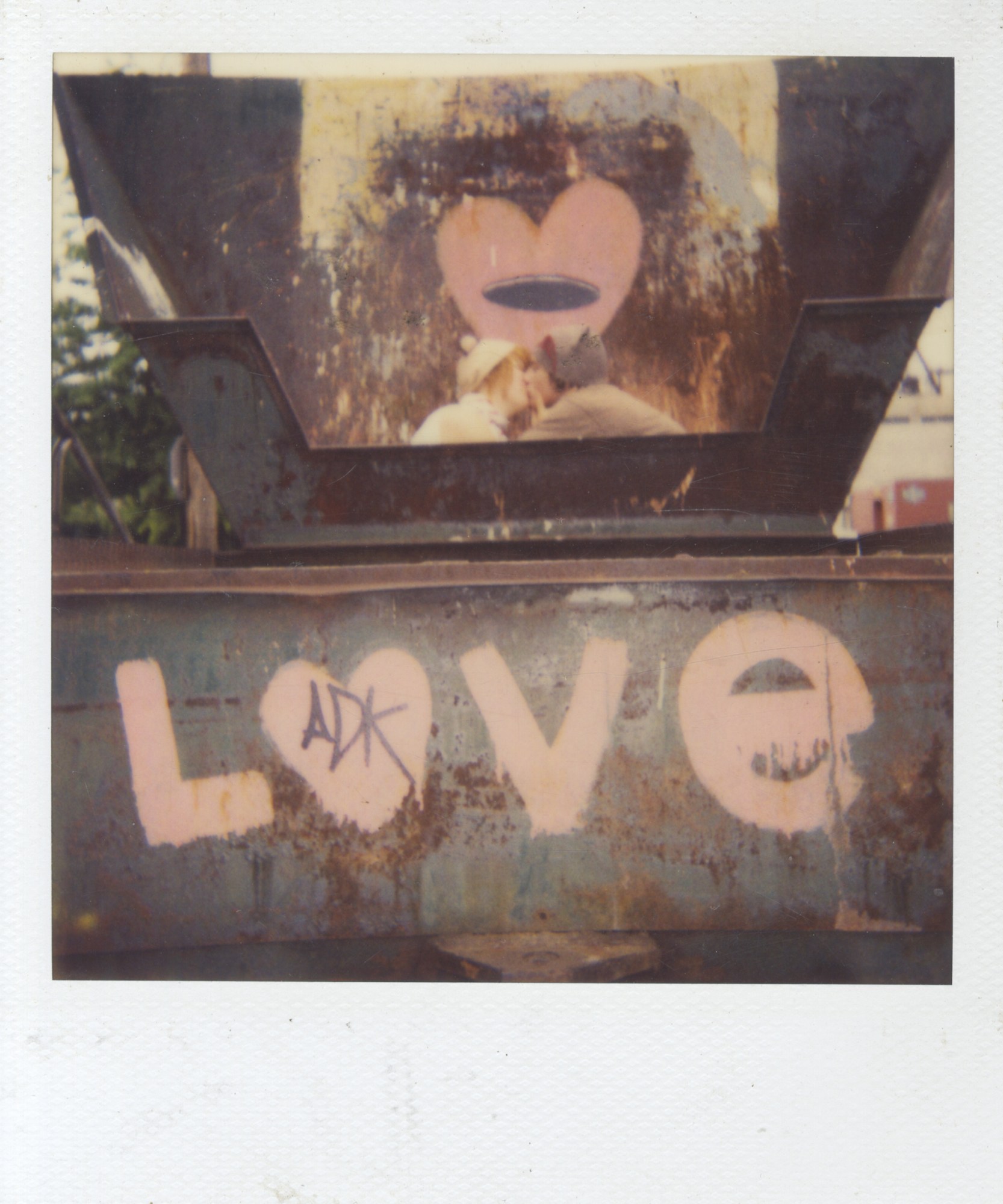 polaroid of a couple kissing in an industrial setting with 'love' in graffiti below them