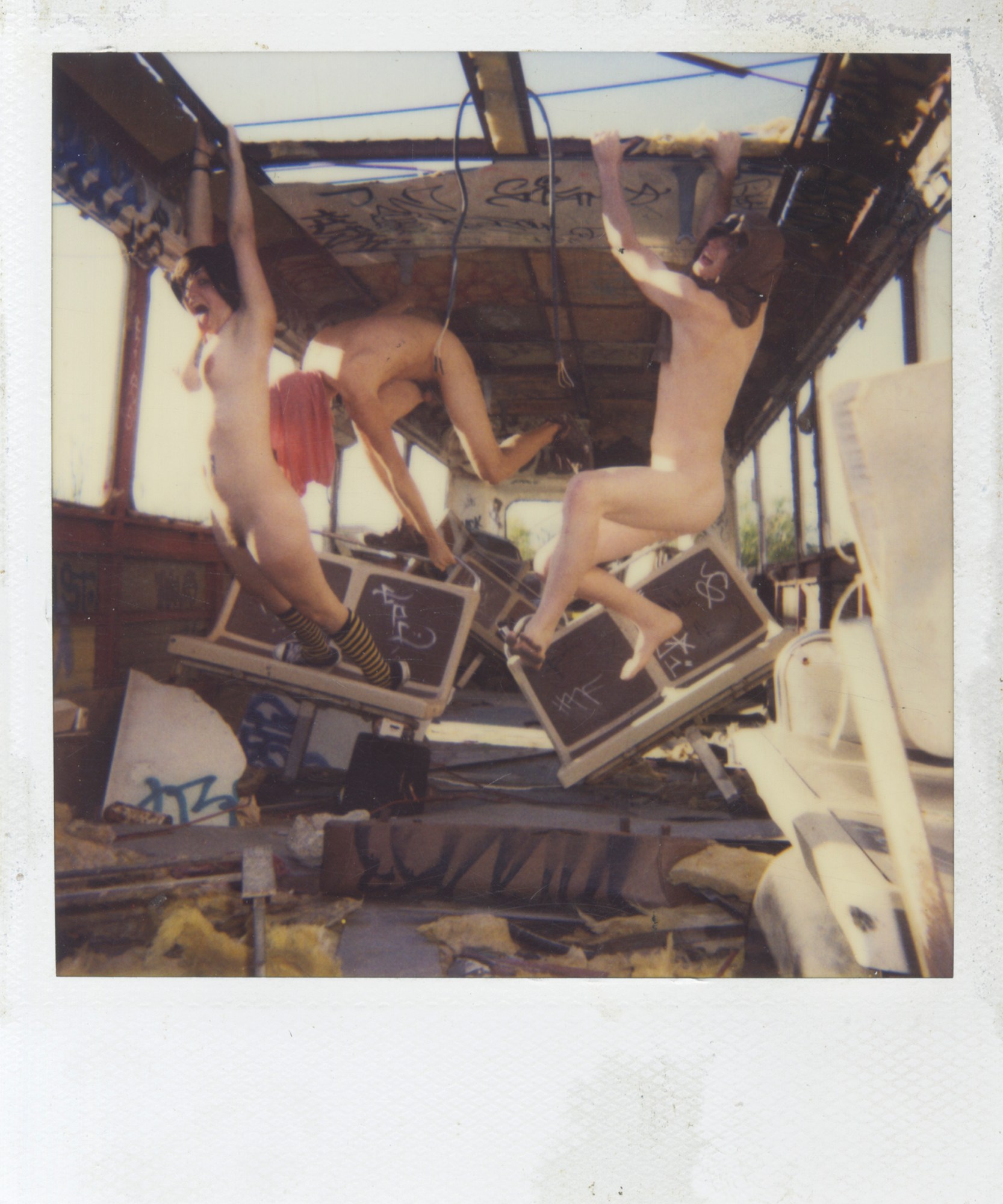 polaroid of 3 nude models hang from the rafters of a broken-down train carriage