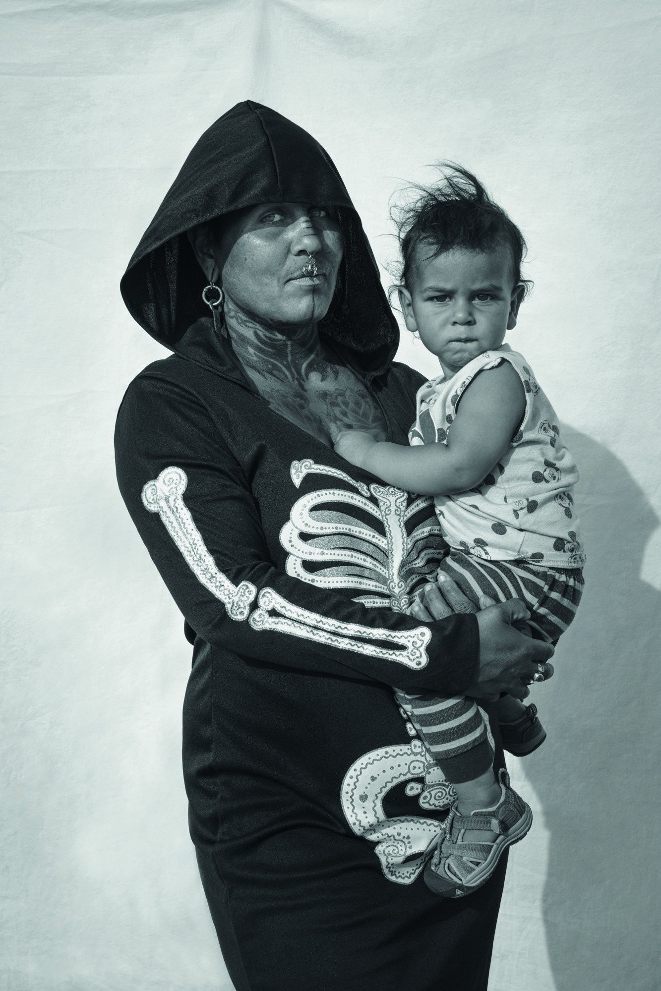 a woman in a skull sweatshirt with piercings and tattoos holding a small child