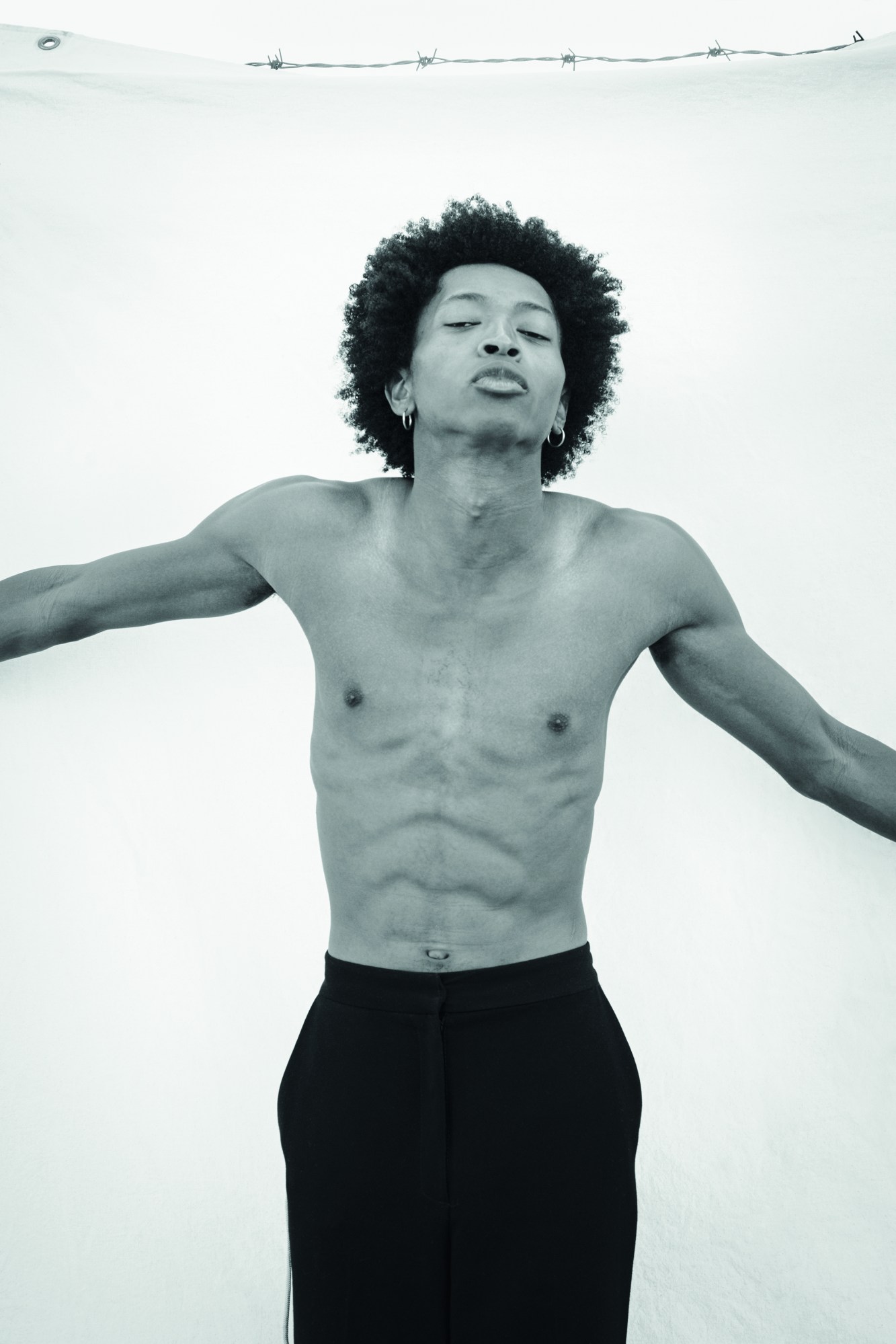 a young black man with an afro shirtless wearing black pants